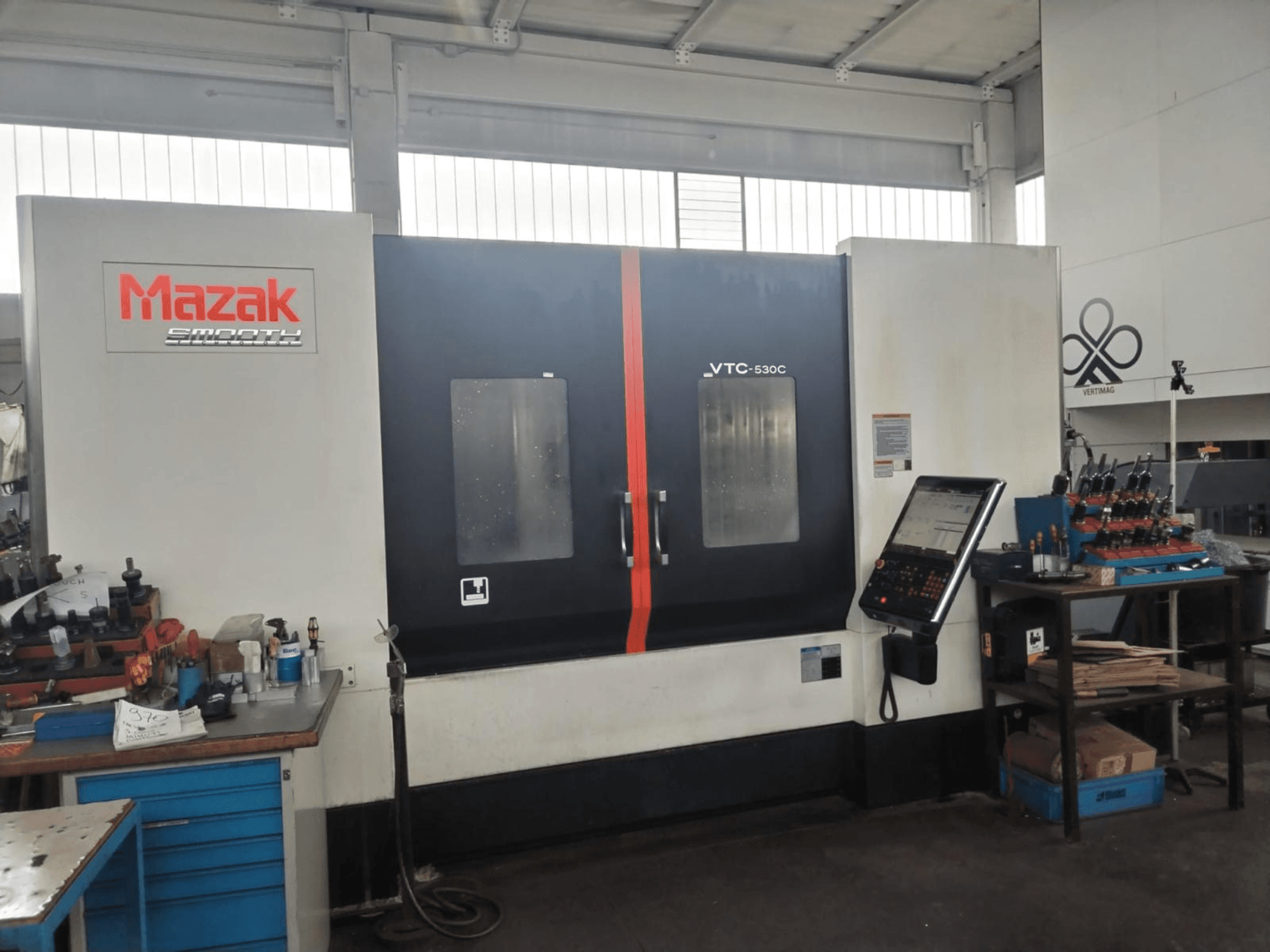 Vertikales Bearbeitungszentrum Mazak VTC-530C in einer Werkstatt, mit einem Bedienfeld und Werkzeugen auf einem Seitentisch.