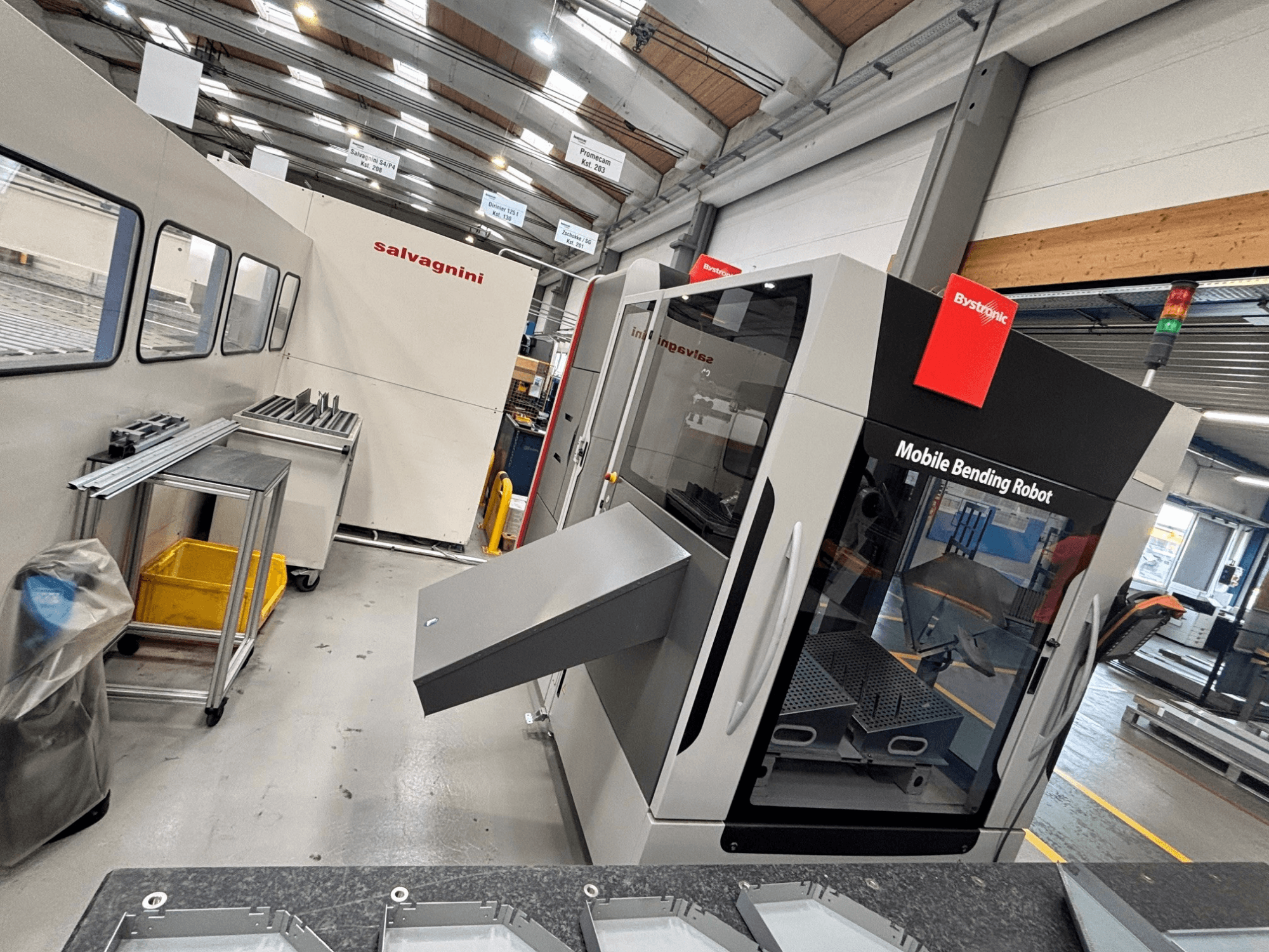 Abkantpresse Bystronic Xpert 40/1030, Vorderansicht mit mobilem Biegeroboter und Arbeitsbereich mit Metallteilen auf einem Tisch.