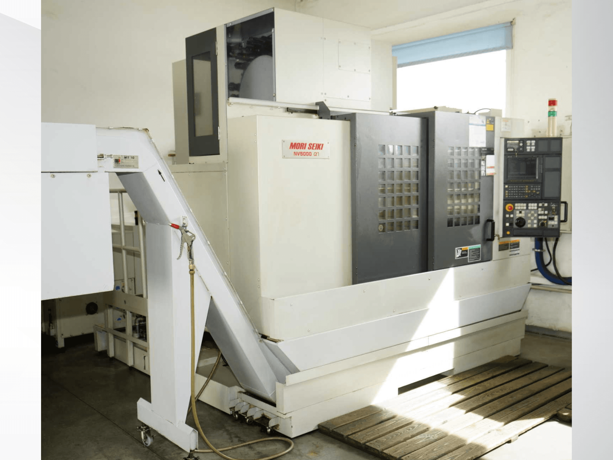 Vertikales Bearbeitungszentrum MORI SEIKI NV 5000 alpha1 in der Vorderansicht mit Blick auf das Bedienfeld, die Sicherheitsvorrichtungen und den Beladungsbereich.