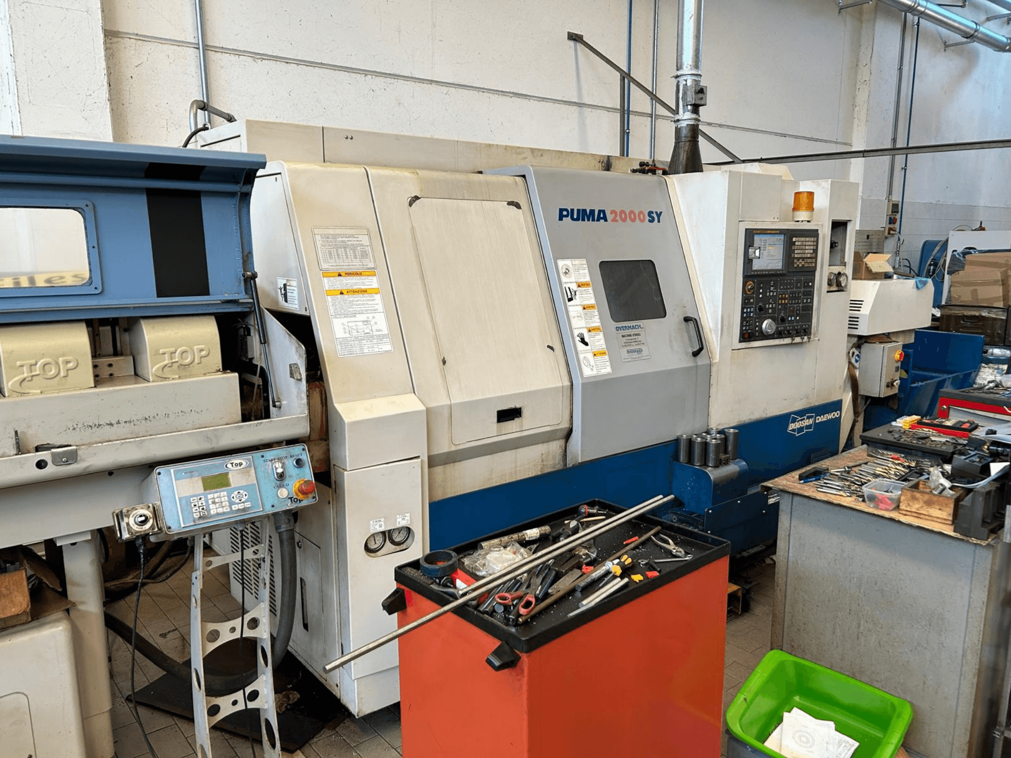 Horizontaldrehmaschine DOOSAN PUMA 2000SY in einer Werkstatt, Seitenansicht mit Blick auf das Bedienfeld und die daneben liegenden Werkzeuge.