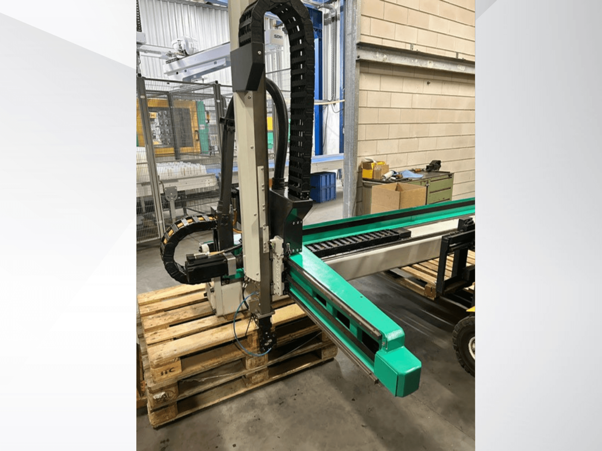 Arburg Multilift Select 15kg quer, Seitenansicht des Werkstückträgers auf Holzpaletten, mit Roboterarm und Steuerungskomponenten.