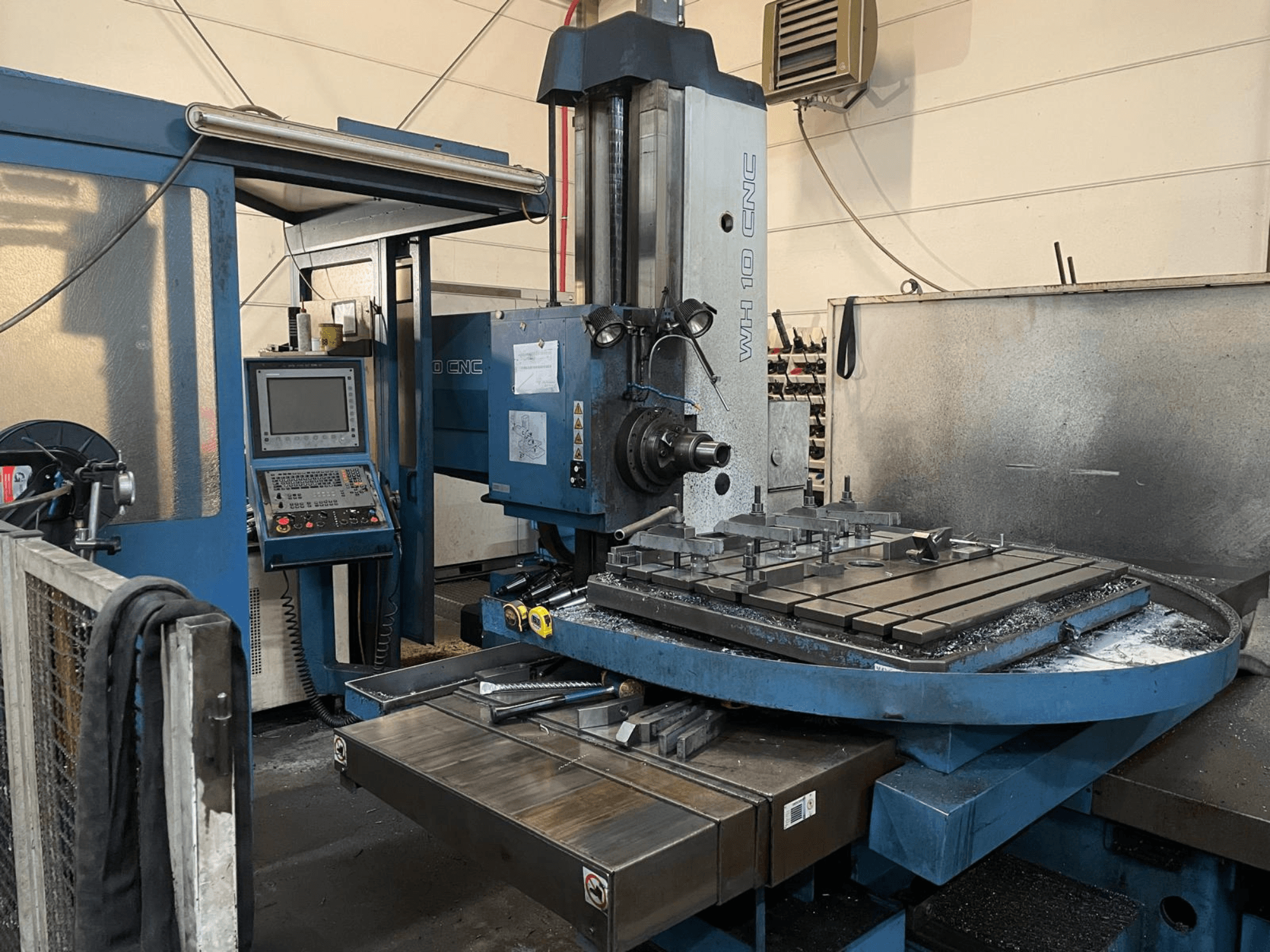TOS WH 10 CNC-Bohrmaschine in einer Werkstatt, Seitenansicht mit Bedienfeld, Arbeitstisch mit Spannvorrichtungen und Metallspänen.