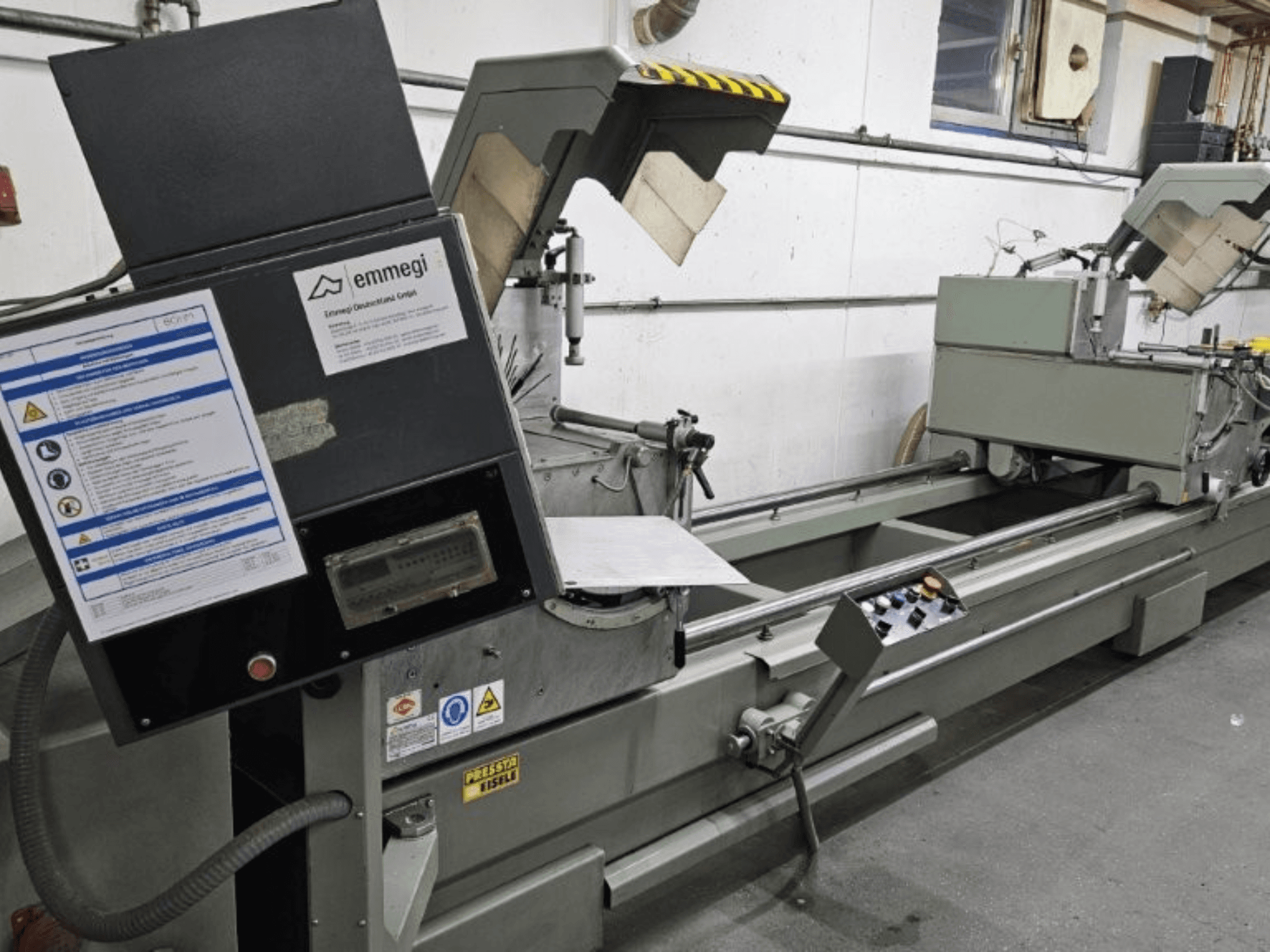 Industrielle Schneidemaschine von Emmegi, Vorderansicht, mit Bedienfeld, Sicherheitsschildern und Betriebskomponenten.