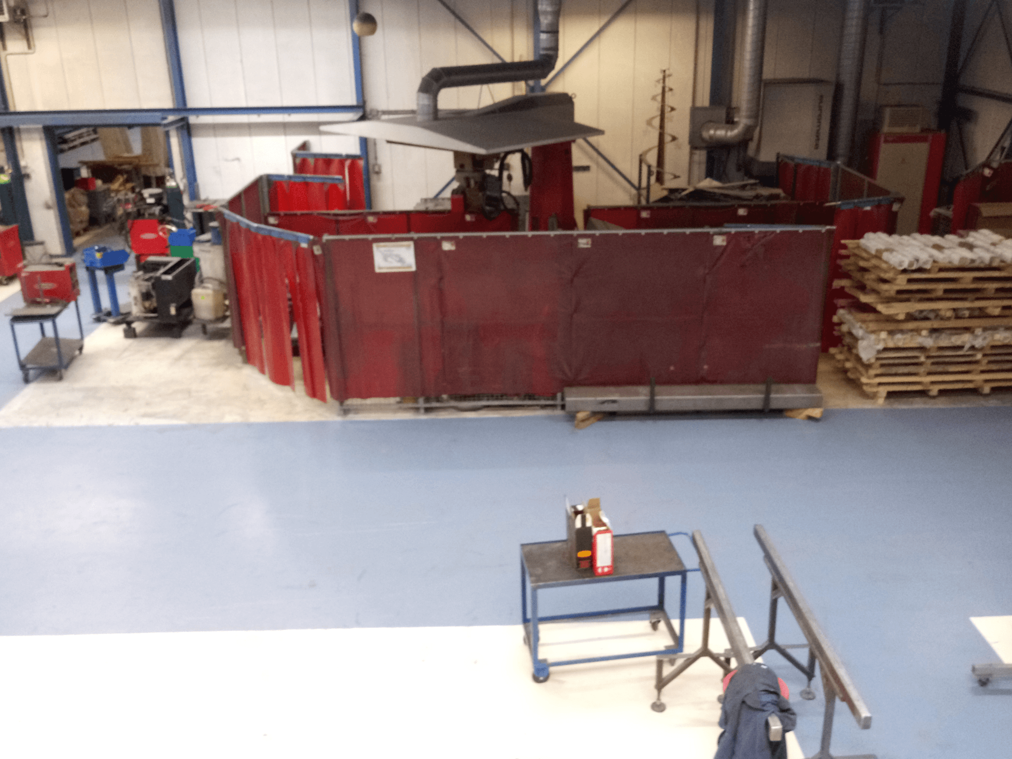 Industrieller Arbeitsbereich mit roten Schweißvorhängen, Maschinen und Paletten; Draufsicht, die die Anordnung und Ausrüstung zeigt.