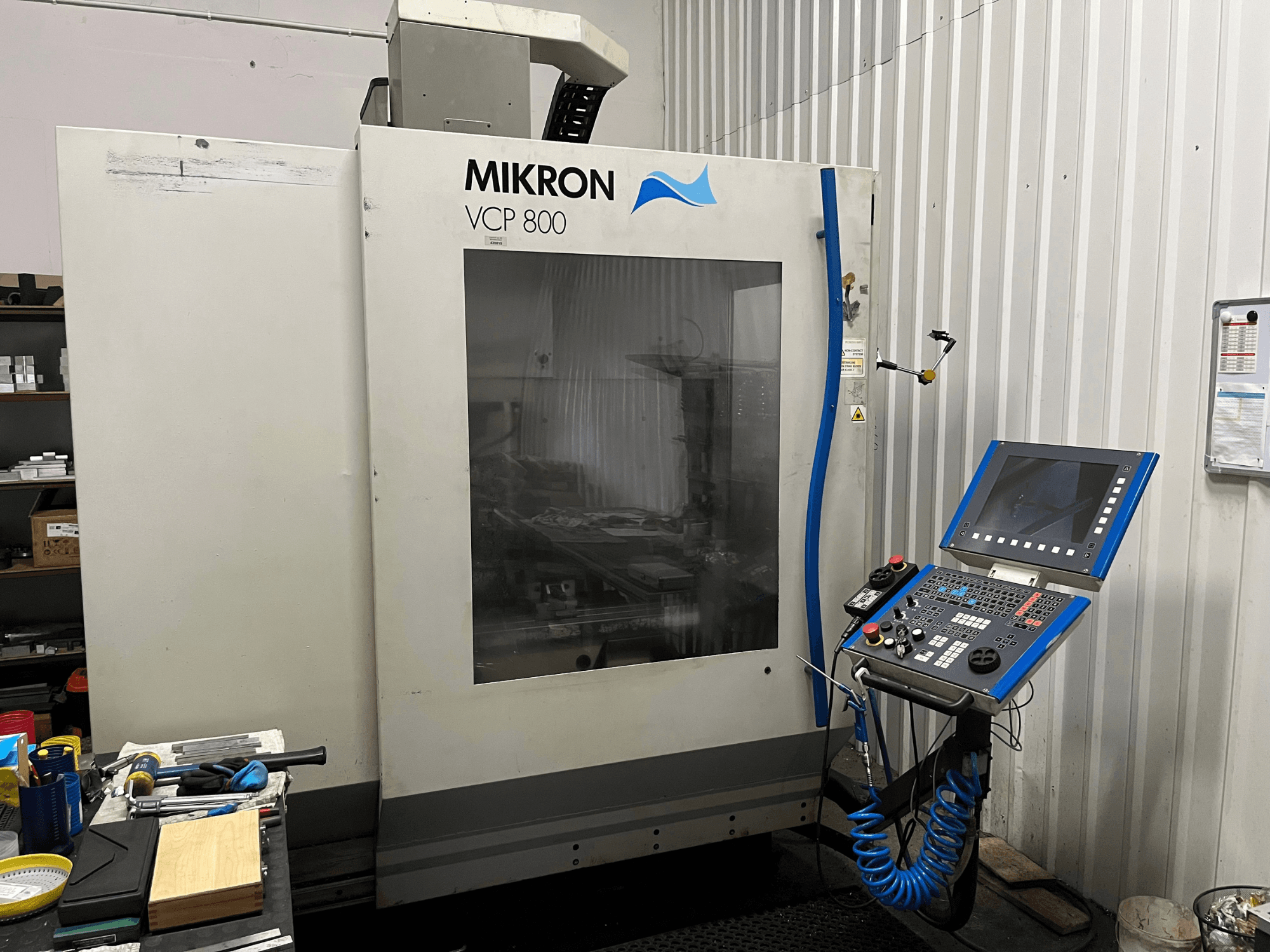 Vertikales Bearbeitungszentrum MIKRON VCP 800, Vorderansicht, mit Bedienfeld und Werkzeugen auf einer Werkbank im Vordergrund.