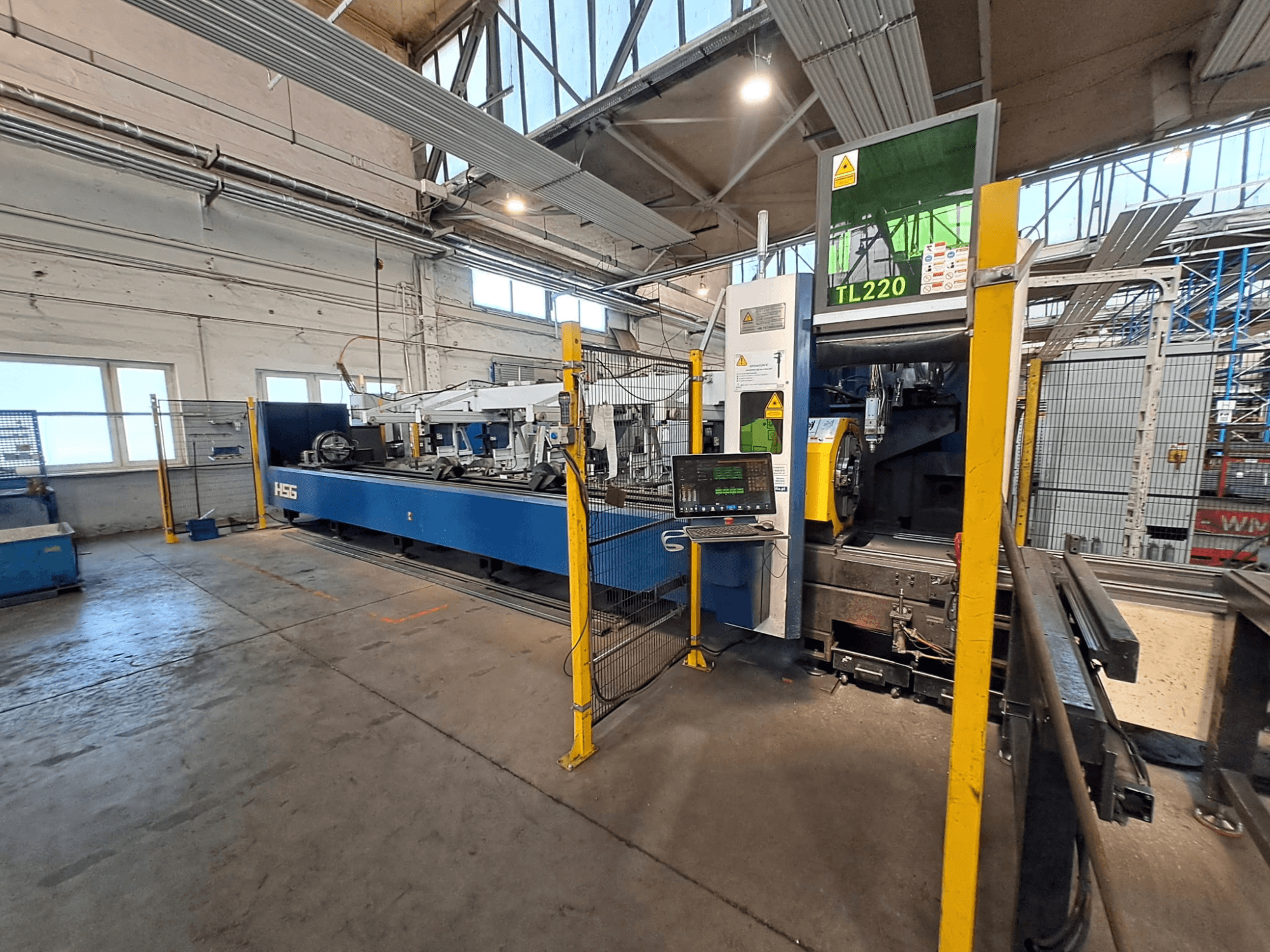 Vorderansicht der Rohrschneidemaschine HSG HS-TL220 mit Bedienfeld und Sicherheitsbarrieren in einer Fabrikumgebung.