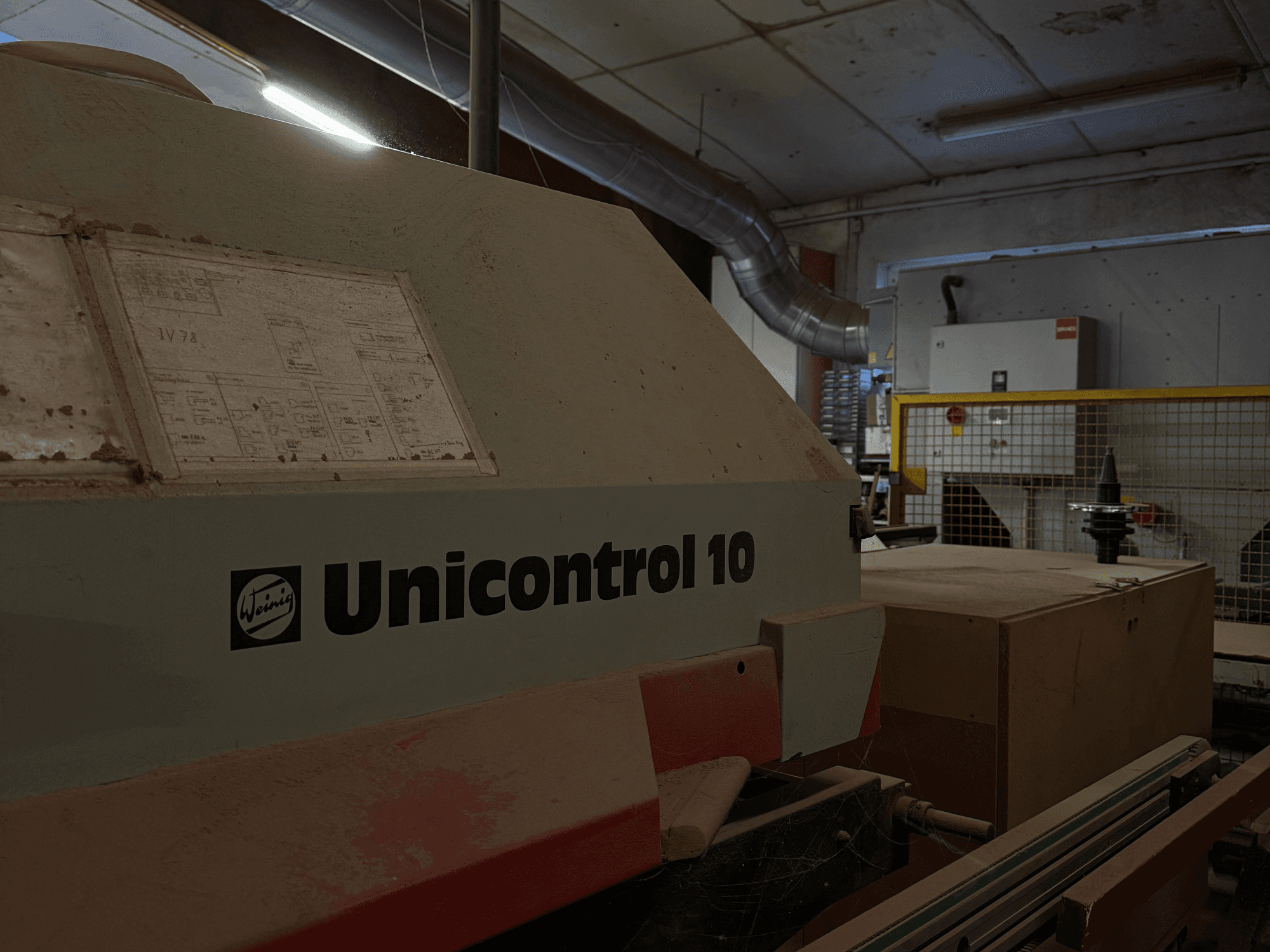 Weinig Unicontrol 10 Maschine von der Seite gesehen, staubige Oberfläche, technische Schaltpläne auf der Frontplatte sichtbar.