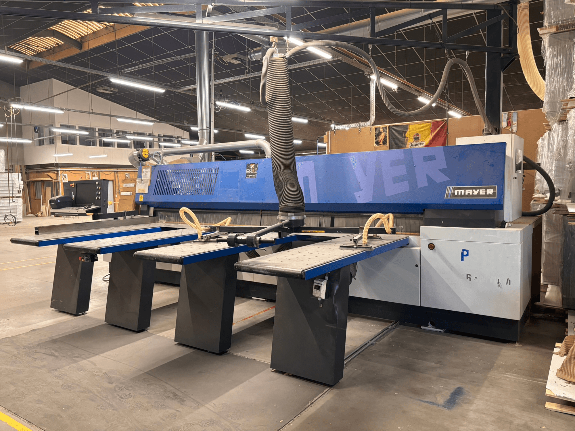 Mayer CNC-Maschine mit blauen Paneelen, Vorderansicht; mit mehreren Arbeitstischen und einer Staubabsaugung für die Holzbearbeitung.
