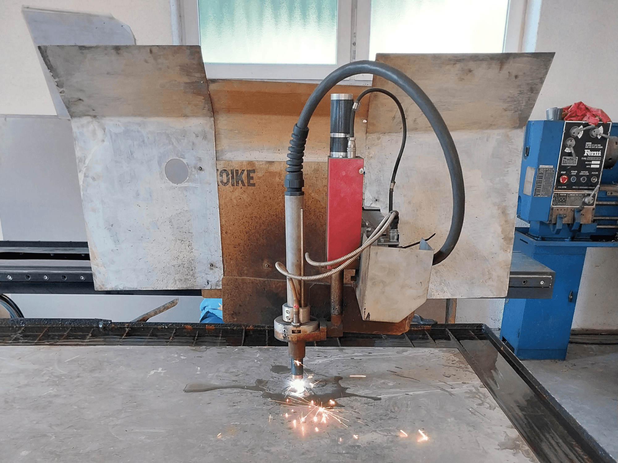 Frontansicht eines Plasmaschneiders von Oike mit Funkenflug, positioniert über einer Metalloberfläche auf einem Arbeitstisch.