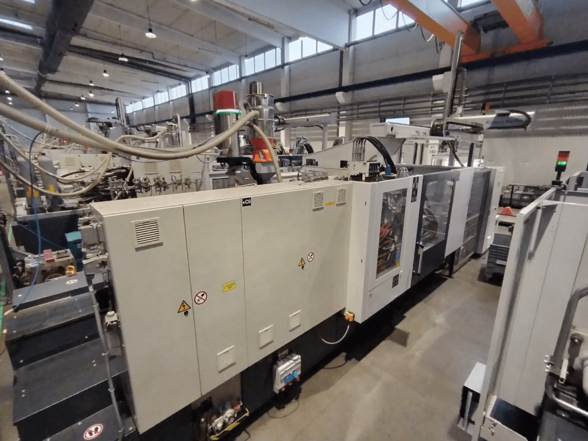 Industrielle Spritzgießmaschine in der Seitenansicht, mit Bedienfeld und Sicherheitshinweisen. Marke: Unbekannt.