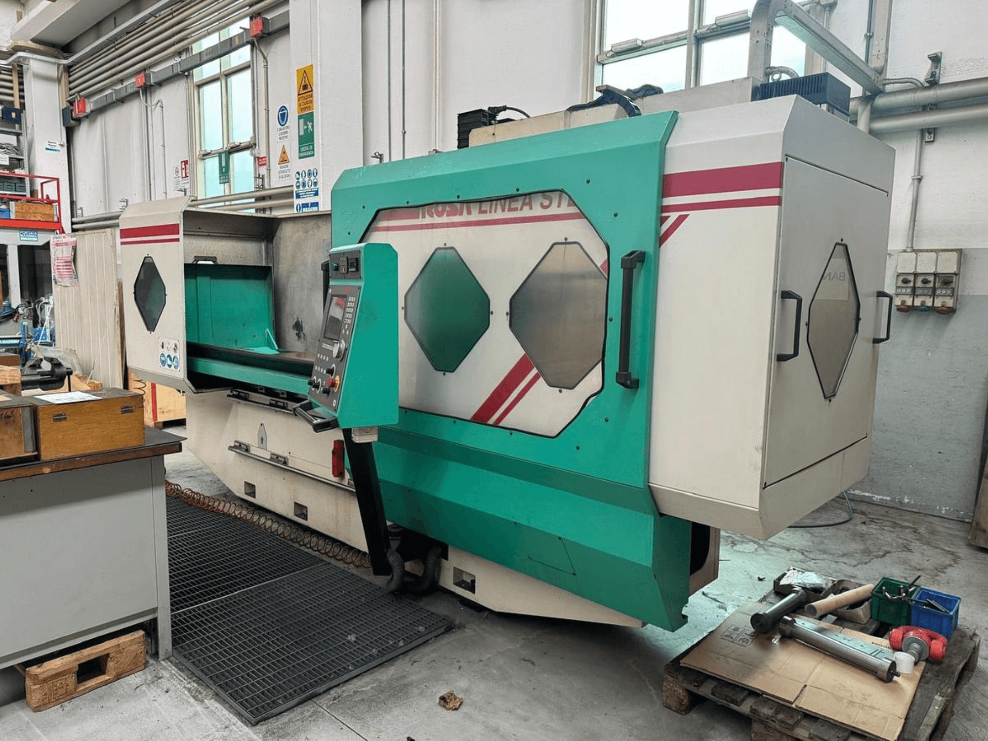 Grün-weiße Präzisionsmaschine, Vorderansicht, mit Bedienfeld, Arbeitsbereich und Werkzeugen auf einer Palette. Marke: BAMB.