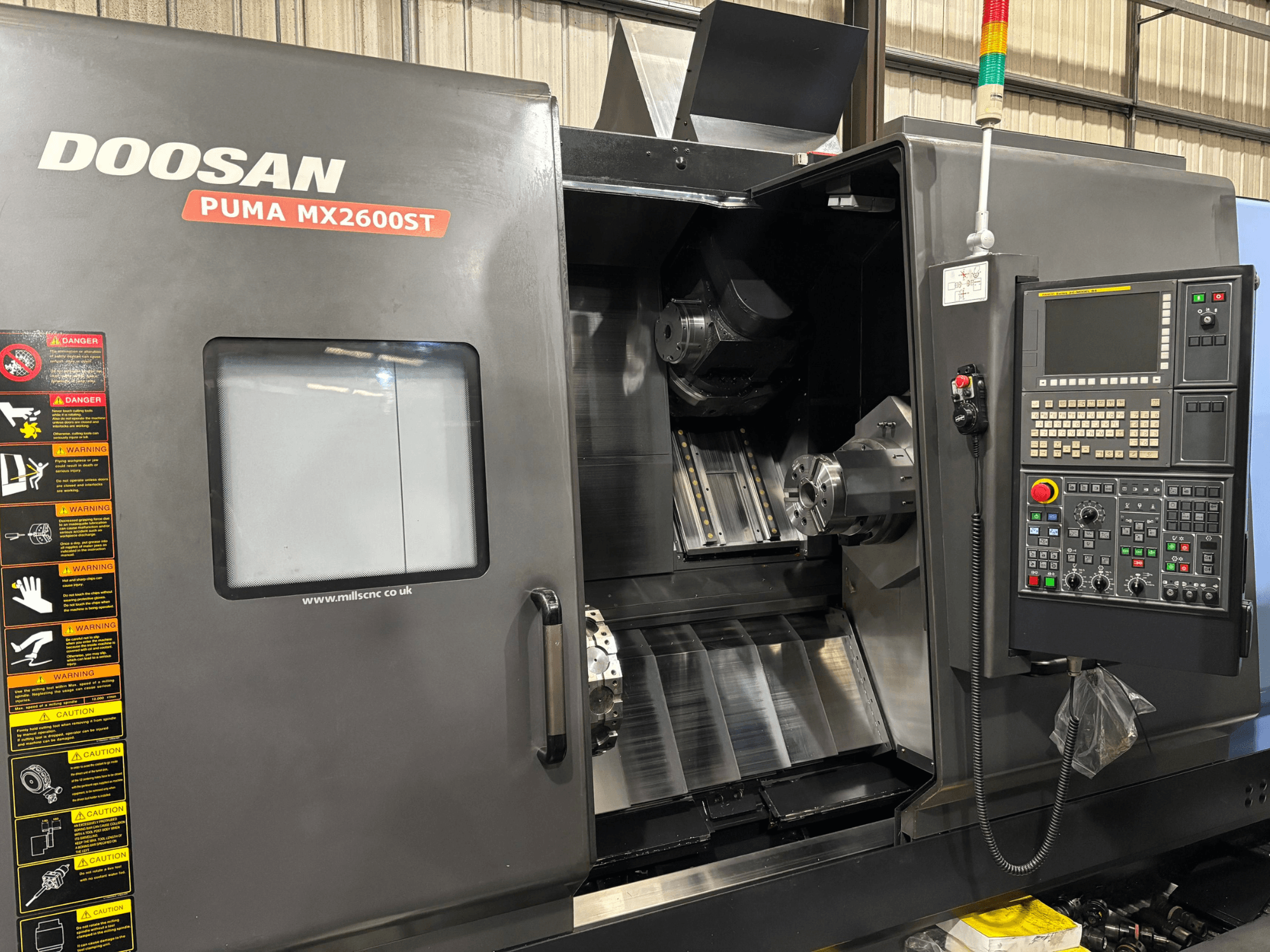 Doosan PUMA MX2600ST CNC-Drehmaschine, Vorderansicht, zeigt Bedienfeld, Spindel und Bearbeitungsbereich mit sichtbaren Sicherheitshinweisen.