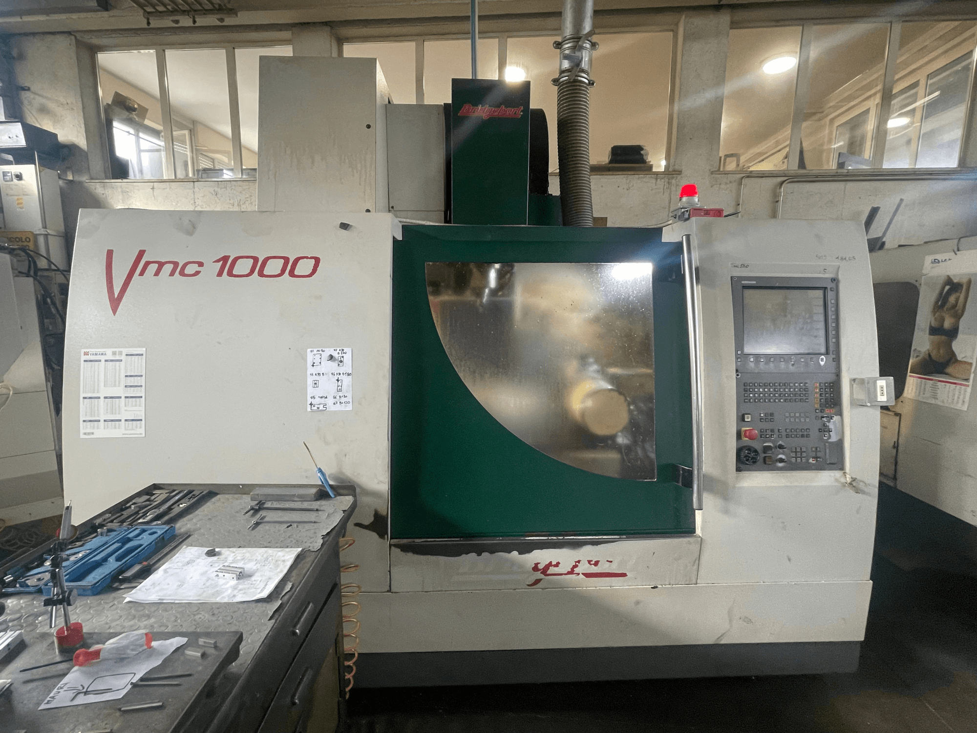 Vertikales Bearbeitungszentrum Bridgeport VMC 1000/30, Vorderansicht, mit Bedienfeld und Hauptkörper, daneben liegen Werkzeuge.
