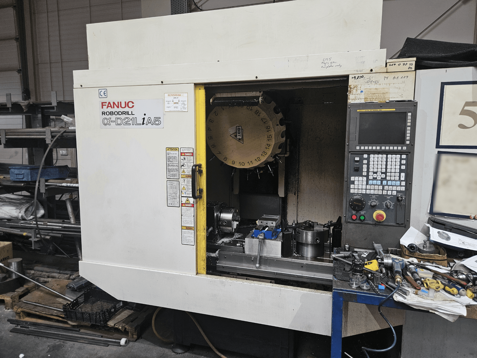 FANUC Robodrill α-D21LiA5, Vorderansicht mit Werkzeughalter und Bedienfeld, umgeben von Werkzeugen und Geräten in einer Werkstatt.