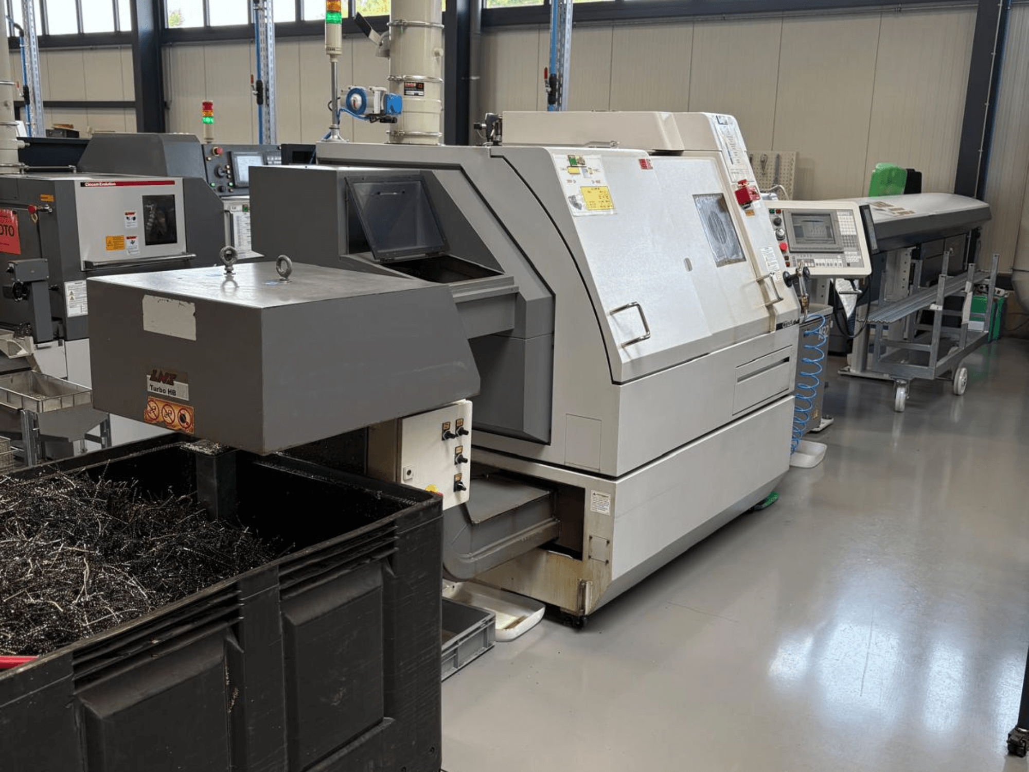 LTA Turbo H8 Industriemaschine, Seitenansicht, mit einem großen Behälter für Metallspäne und Bedienfeld in einer Fabrikumgebung.