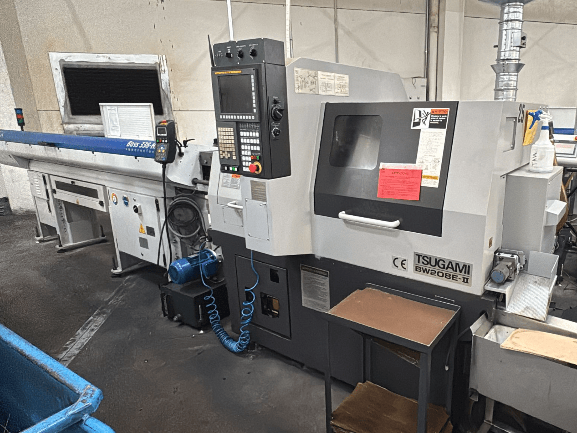 Tsugami BW208E-II CNC-Maschine in einer Werkstatt, von vorne gesehen, mit Bedienfeld und Sicherheitsschildern sichtbar.