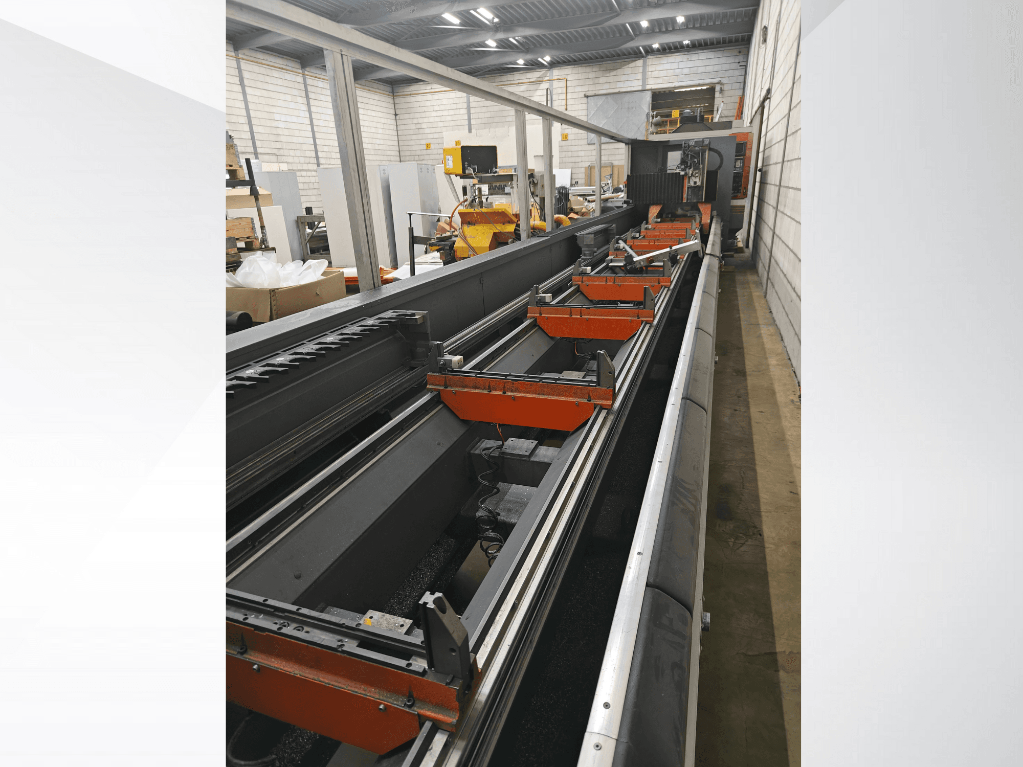 Seitenansicht einer industriellen CNC-Maschine mit Linearschienen, orangefarbenen Klemmen und Präzisionsbauteilen in einer Lagerumgebung.