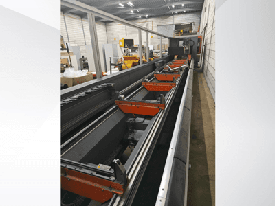 Seitenansicht einer industriellen CNC-Maschine mit Linearschienen, orangefarbenen Klemmen und Präzisionsbauteilen in einer Lagerumgebung.