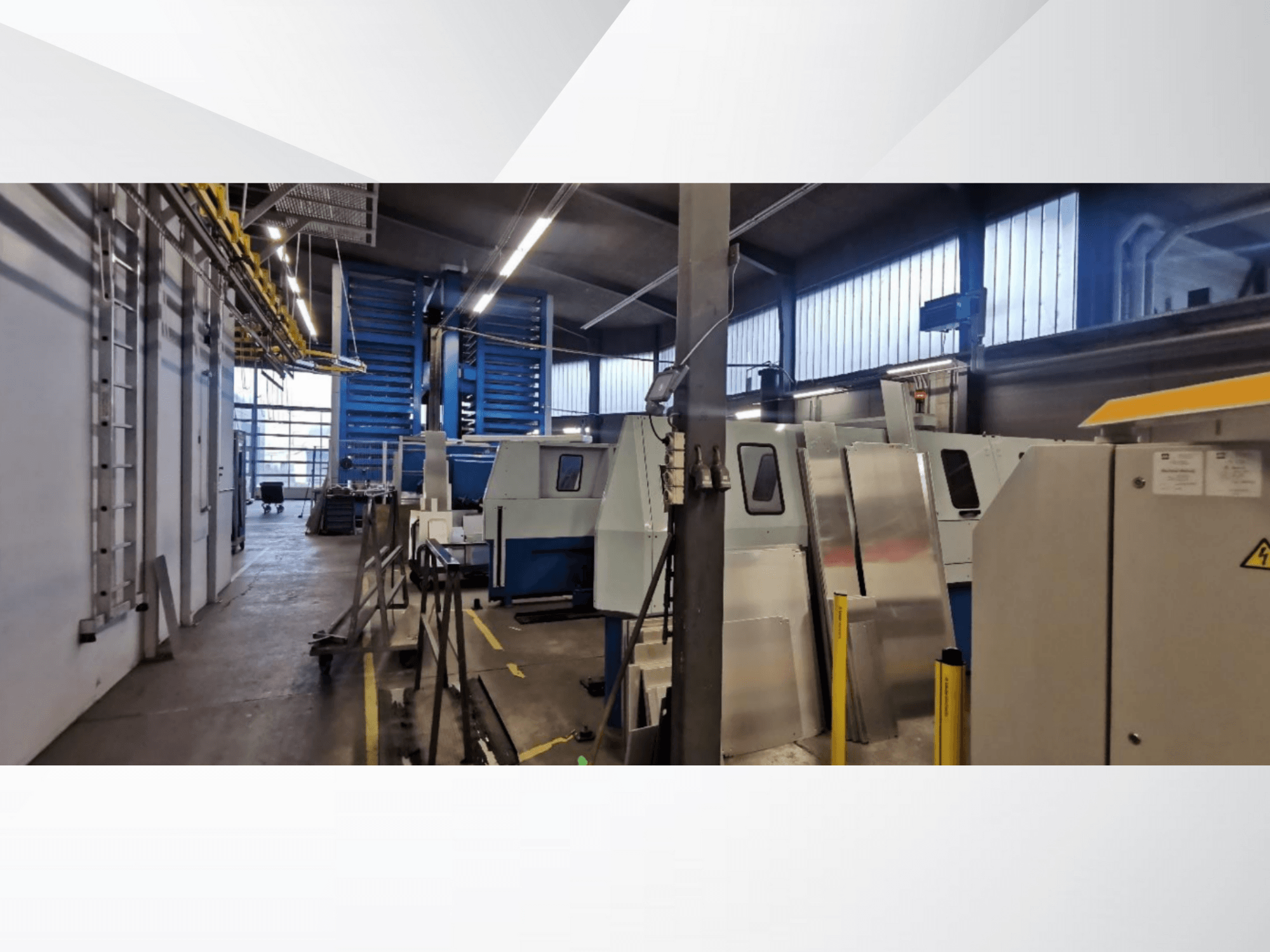 Industrielle Werkstattszene mit mehreren Maschinen und Geräten in einer Seitenansicht, mit metallischen Oberflächen und sichtbaren Sicherheitsvorrichtungen.