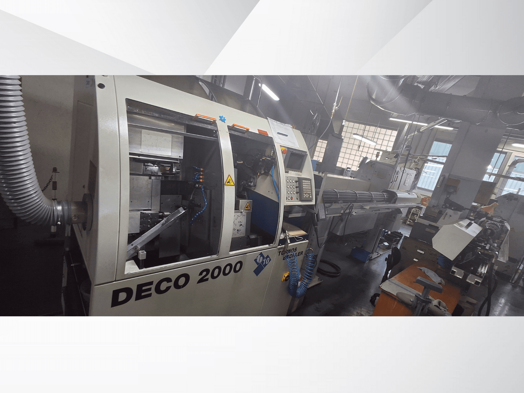 DECO 2000 CNC-Maschine in einer Werkstatt, Vorderansicht mit den Bedienelementen und einer langen Werkstückaufspannung rechts.