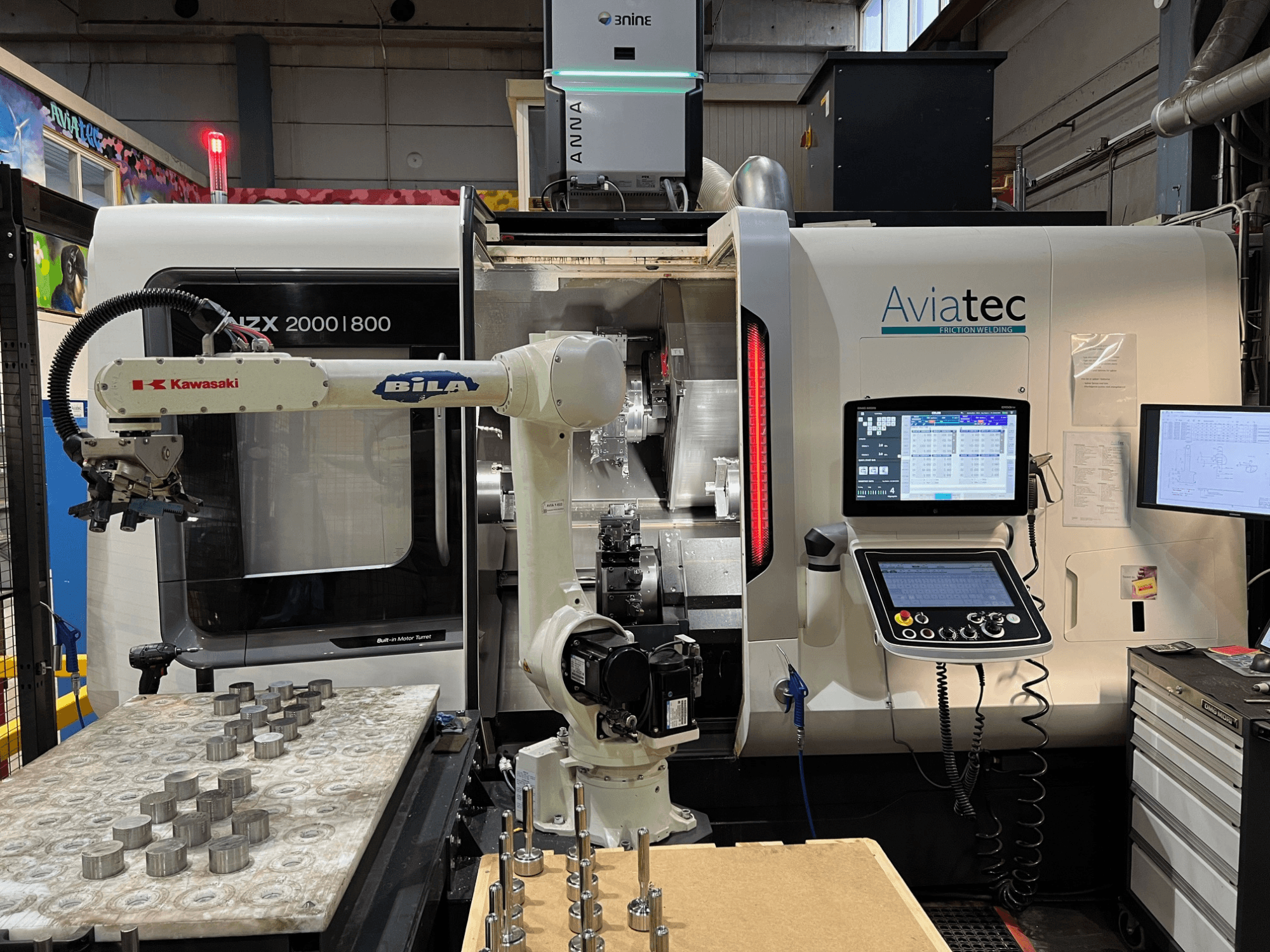 Horizontal-Drehmaschine DMG MORI NZX 2000/800SY mit Kawasaki-Roboterarm, Bedienfeld und Metallbauteilen auf dem Arbeitstisch.