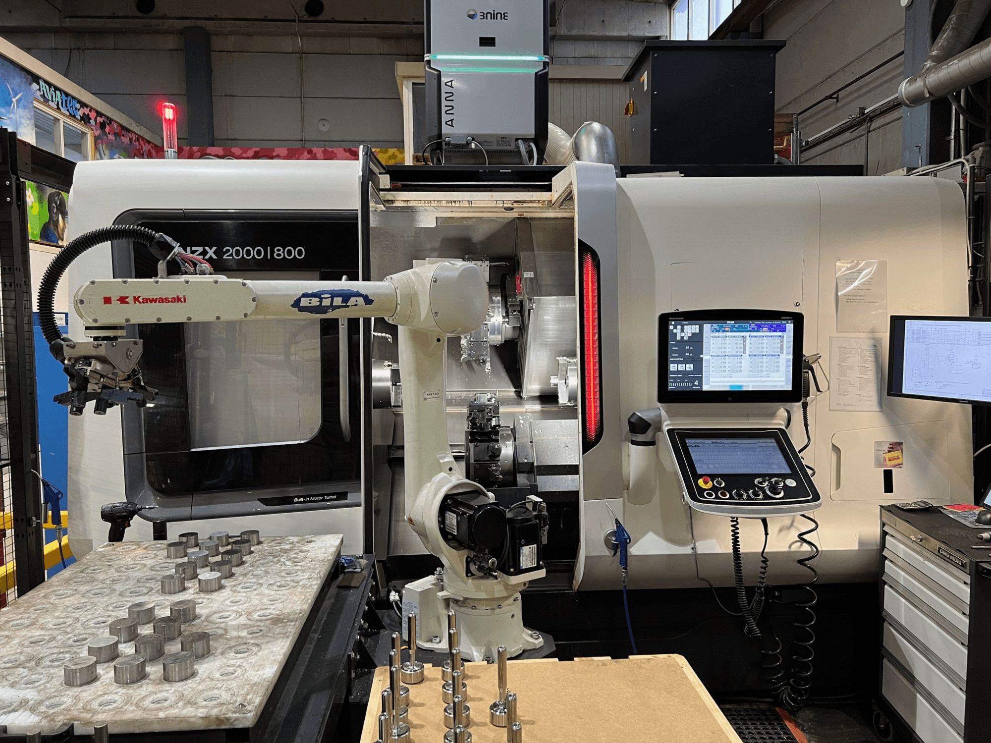 Horizontaldrehmaschine DMG MORI NZX 2000/800SY in einer Werkstatt, mit sichtbarem Kawasaki-Roboterarm und Steuerungselementen.