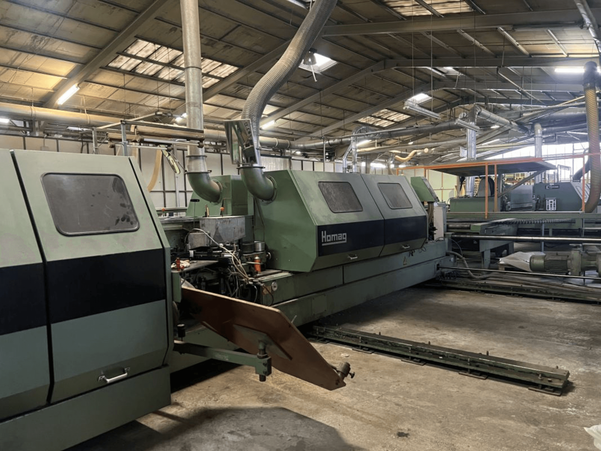 Homag-Industriemaschine in grüner Farbe, Seitenansicht, mit funktionstüchtigen Komponenten und Bedienfeld in einer Lagerumgebung.