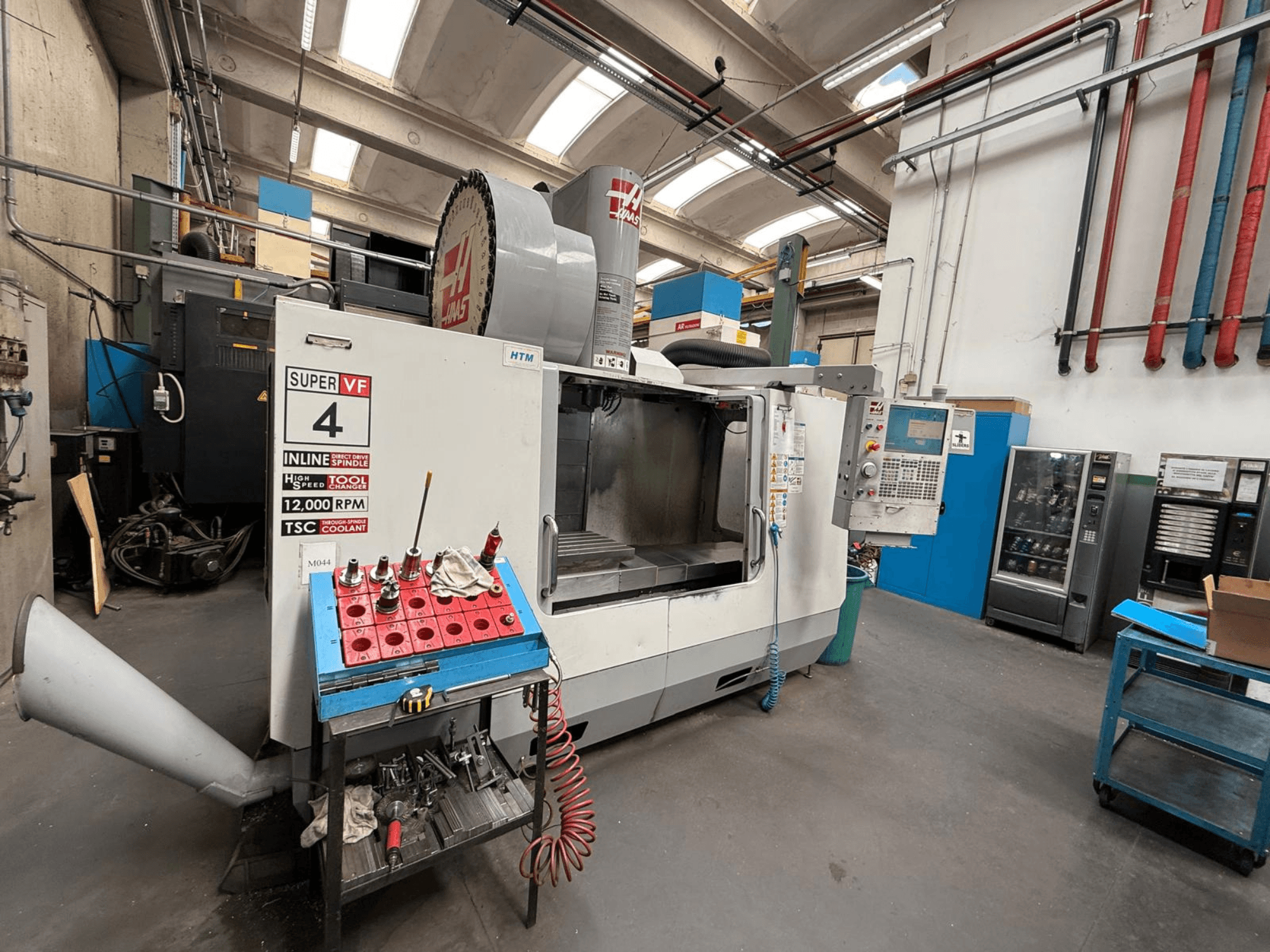 HAAS Super VF 4 CNC-Fräsmaschine mit Bedienpult, Spindel mit 12.000 U/min und Werkzeugen auf einem blauen Lagerregal, Seitenansicht.