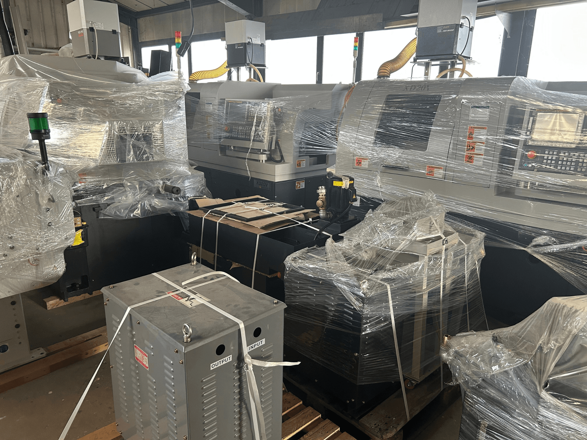 Hanwha XD20 Schweizer Drehmaschine, Vorderansicht, in Kunststoff verpackt, zeigt Bedienfeld und Anbaugeräte in einer Lagerumgebung.