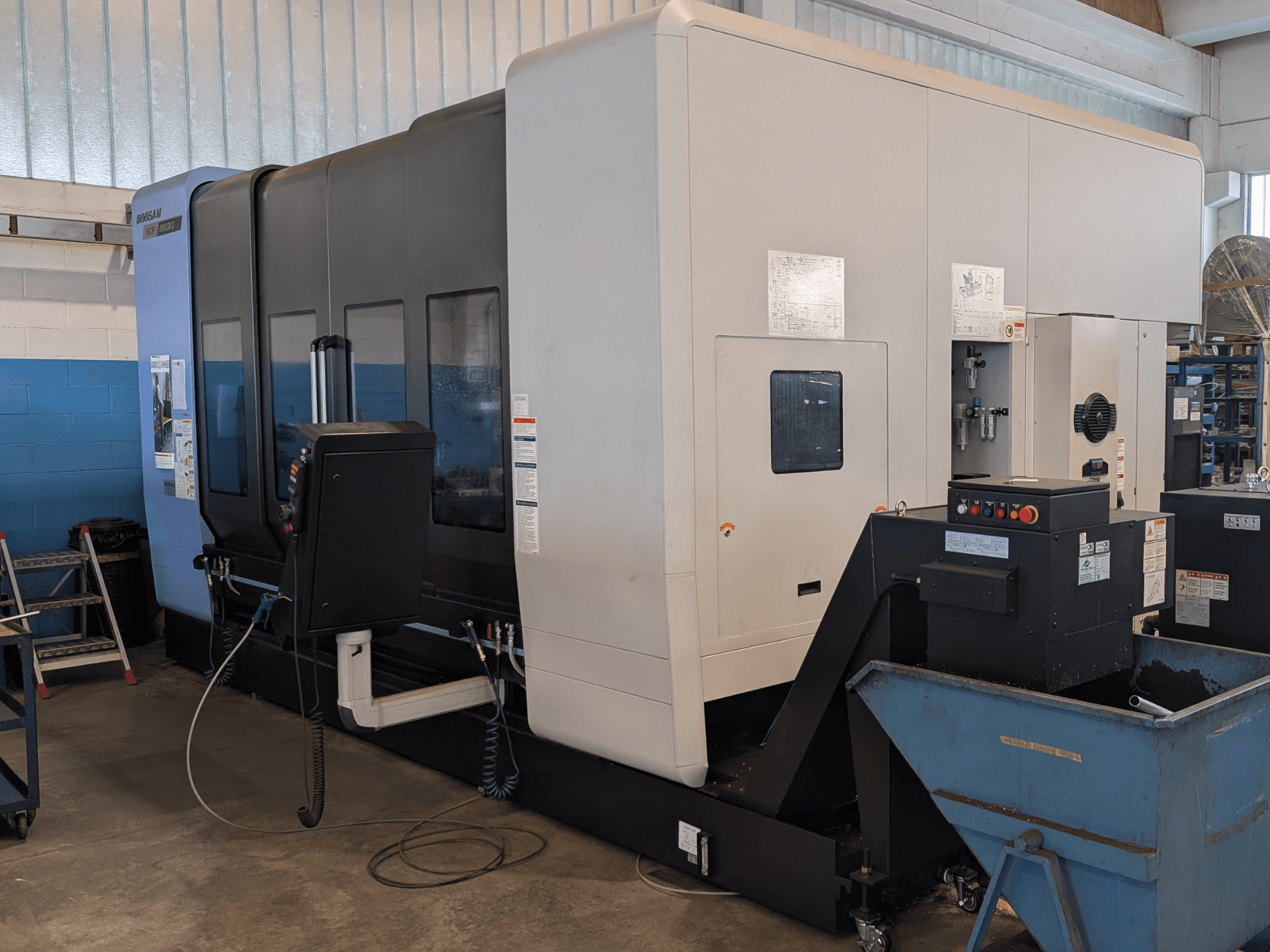 Das vertikale Bearbeitungszentrum DOOSAN VCF850LSR-II in Seitenansicht, mit Blick auf das Bedienfeld, das Kühlmittelsystem und die robuste Bauweise.