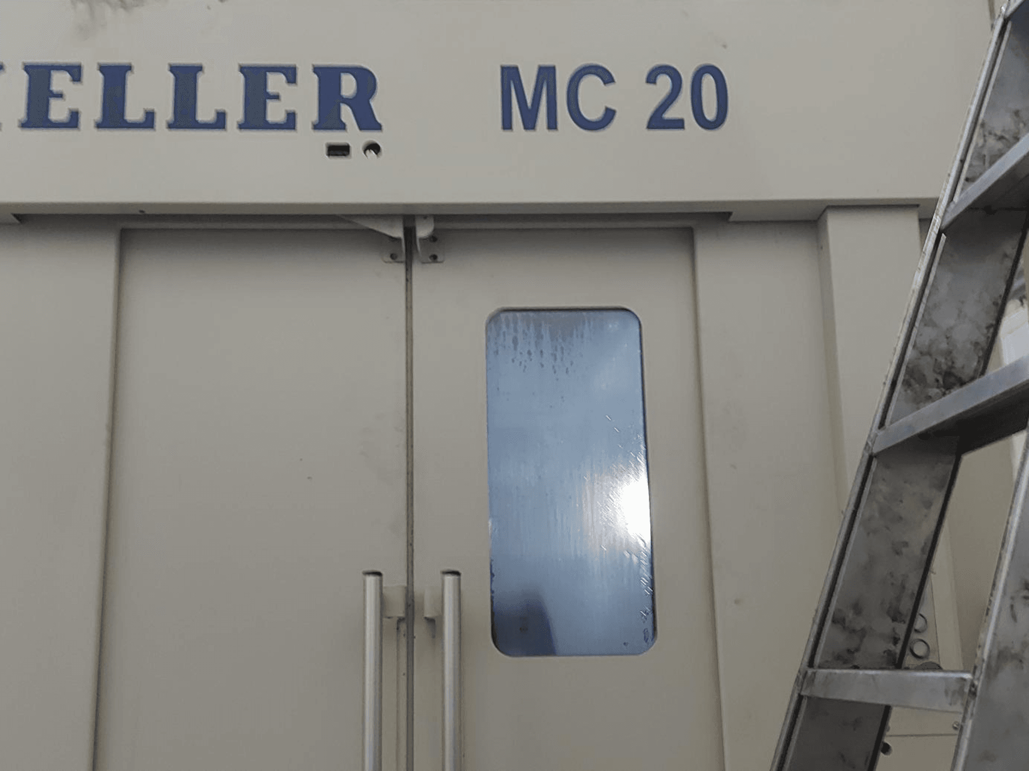 Frontansicht des horizontalen Bearbeitungszentrums HELLER MC 20, mit Türgriffen und einem kleinen Fenster. Leiter an der Seite.