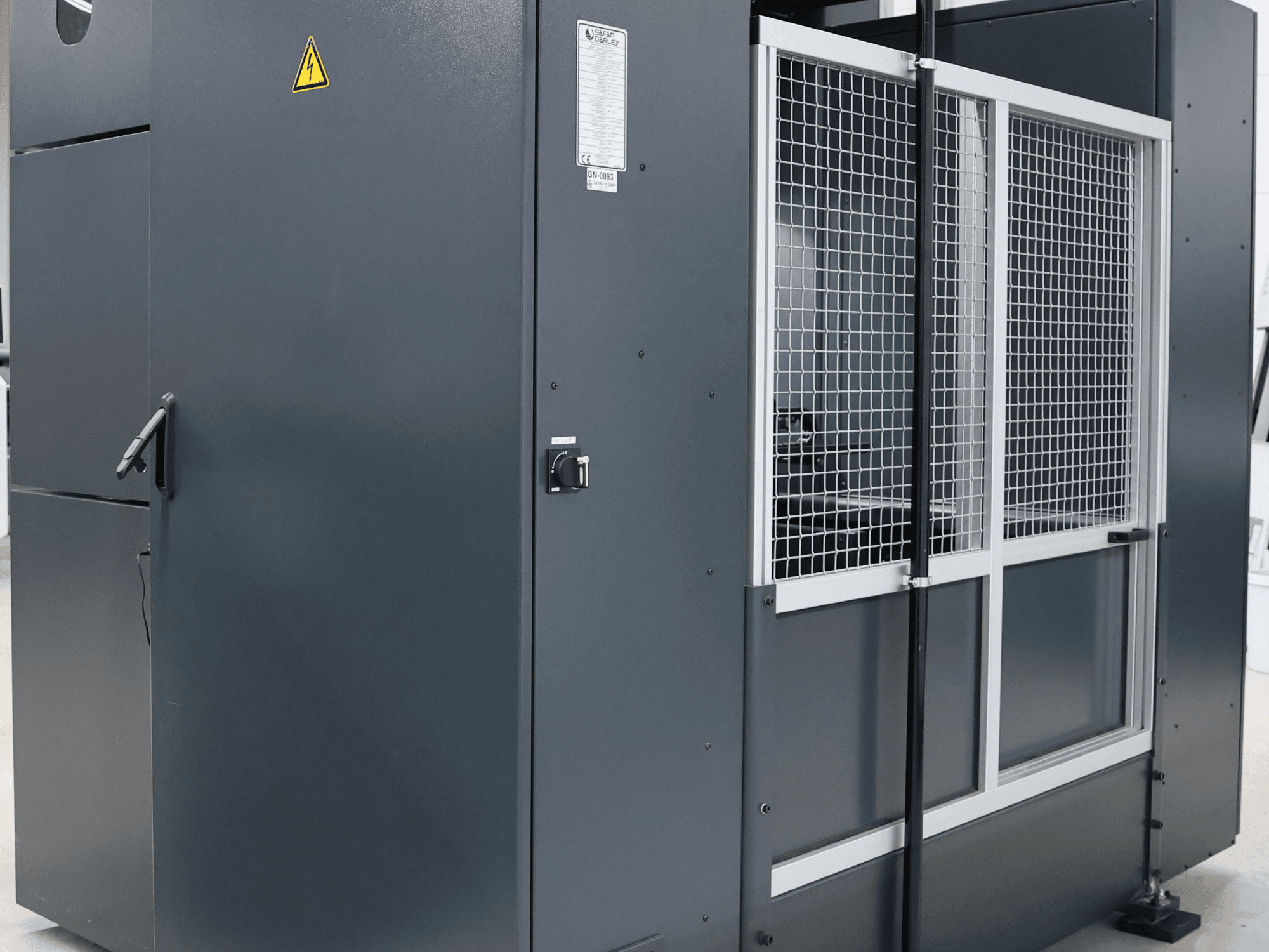 Graue Industriemaschine mit Sicherheitswarnung, Vorderansicht mit Gittertür und Bedienfeld, Modell beschriftet.