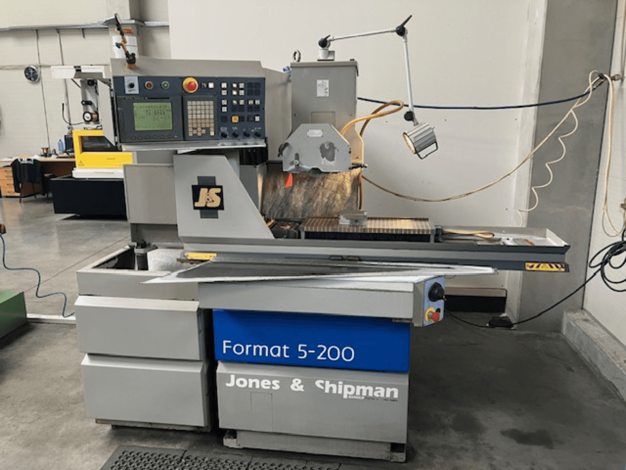 Flachschleifmaschine Jones & Shipman Format 5-200 in Seitenansicht, mit Bedienfeld, Schleifscheibe und Arbeitstisch.