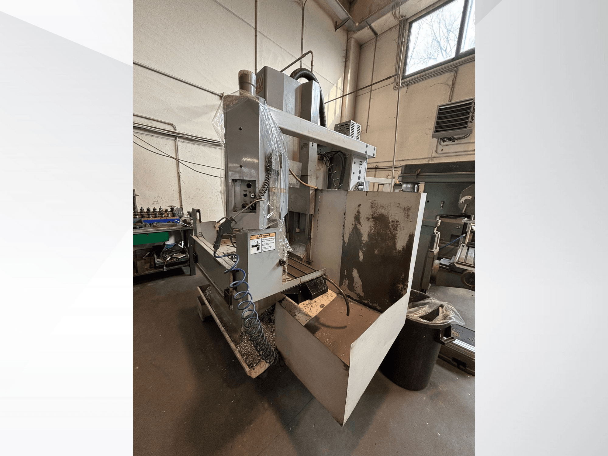 Vertikale Fräsmaschine mit Schutzabdeckung, Seitenansicht; einschließlich Kühlmittelschlauch und Bedienfeld sichtbar. Ideal für die Bearbeitung.