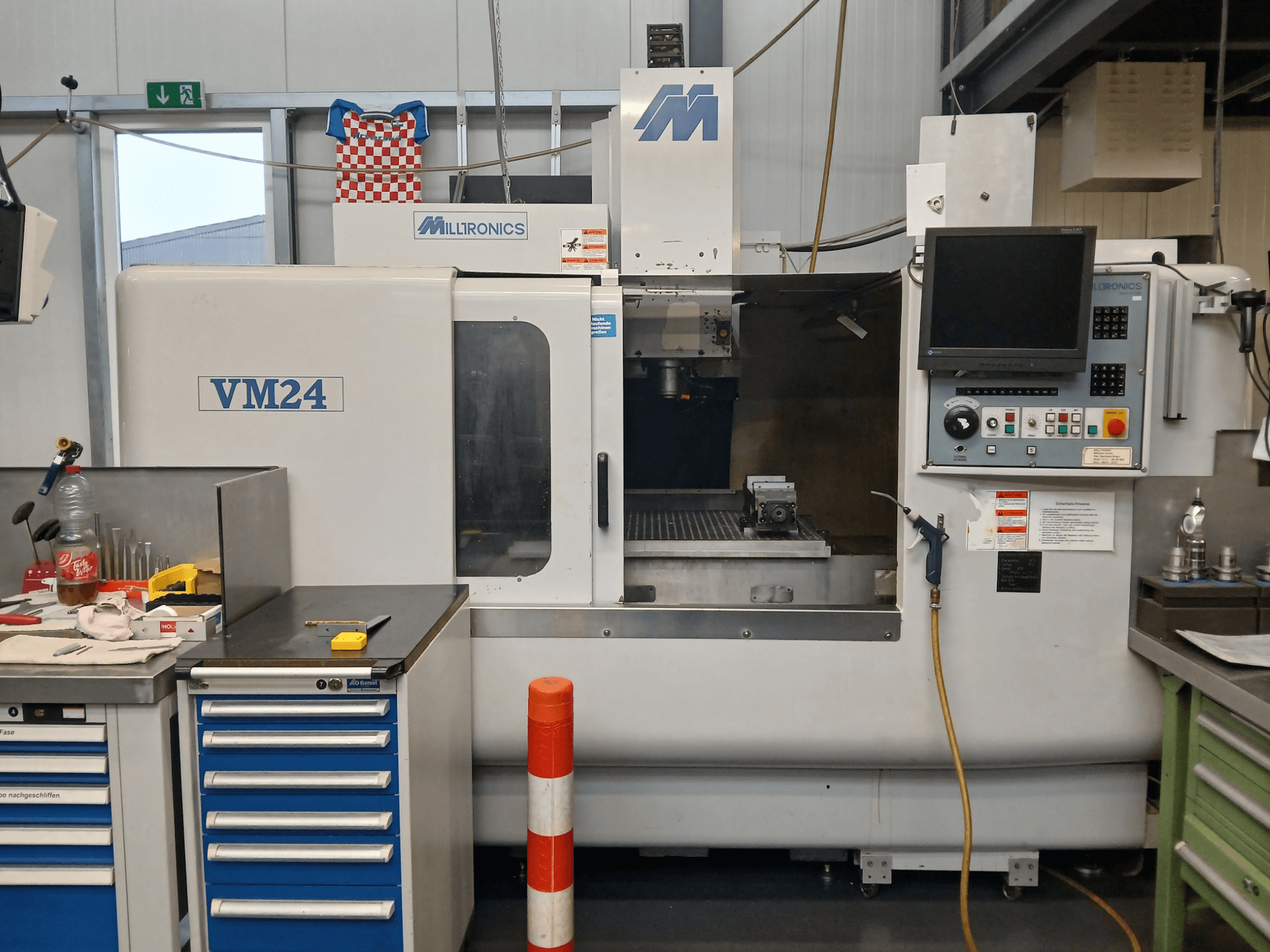 Milltronics VM24 CNC-Fräsmaschine in der Frontansicht mit Bedienfeld, Werkzeugspeicher und Arbeitsraumeinrichtung.