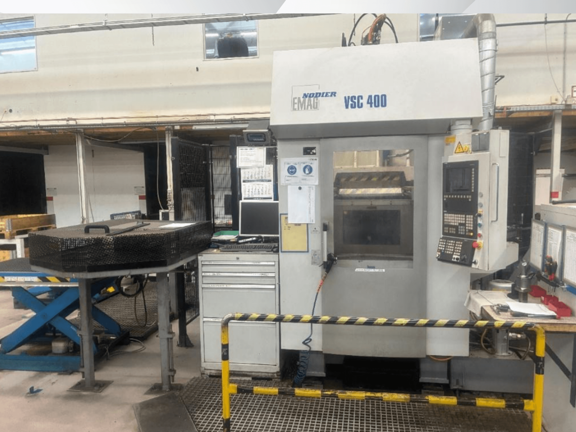 Frontansicht der EMAG VSC 400 Vertikaldrehmaschine mit Bedienfeld, Sicherheitsbarrieren und umgebenden Anlagen in einer gut beleuchteten Werkstatt.