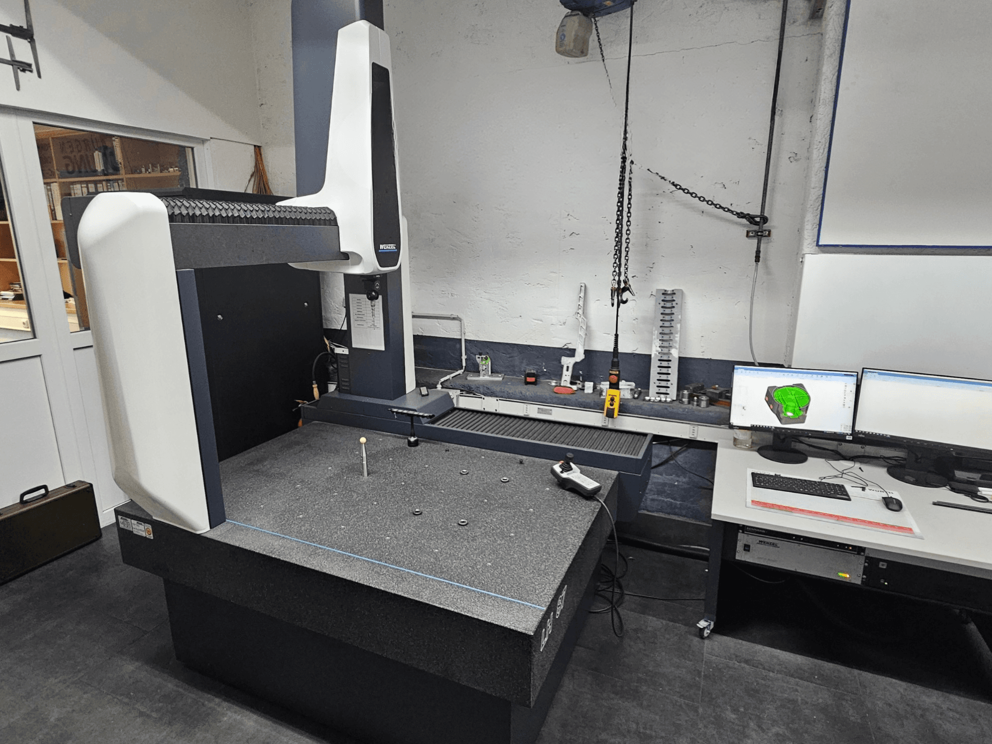 Koordinatenmessgerät Wenzel LH 87 in einer Werkstatt, Vorderansicht, mit einem Messtaster auf dem Granittisch und zwei Monitoren, die die CAD-Konstruktion anzeigen.
