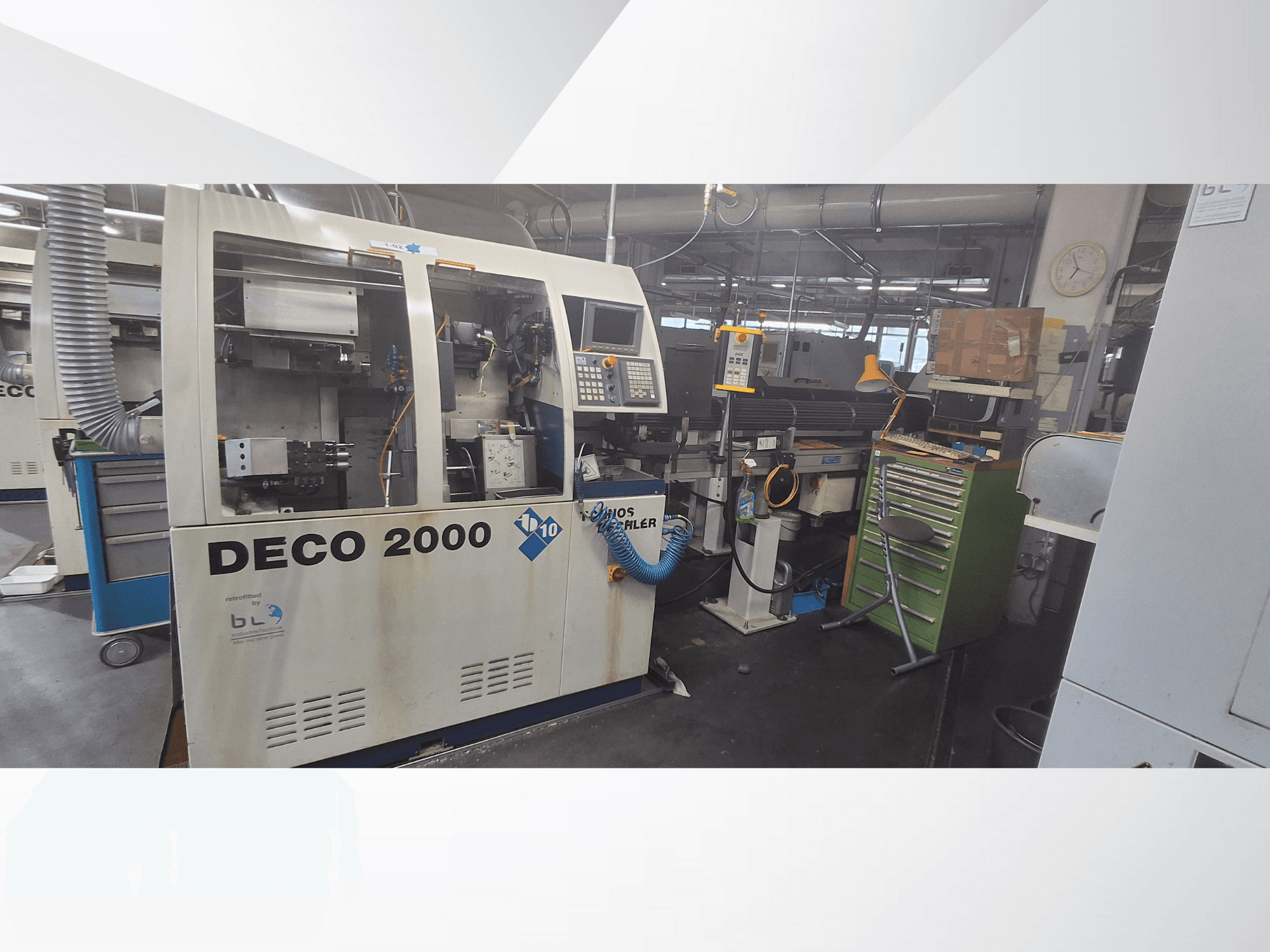 DECO 2000 Maschine von vorne gesehen, mit Bedienfeld, Rohren und einem überfüllten Arbeitsbereich mit Werkzeugen und Kisten.
