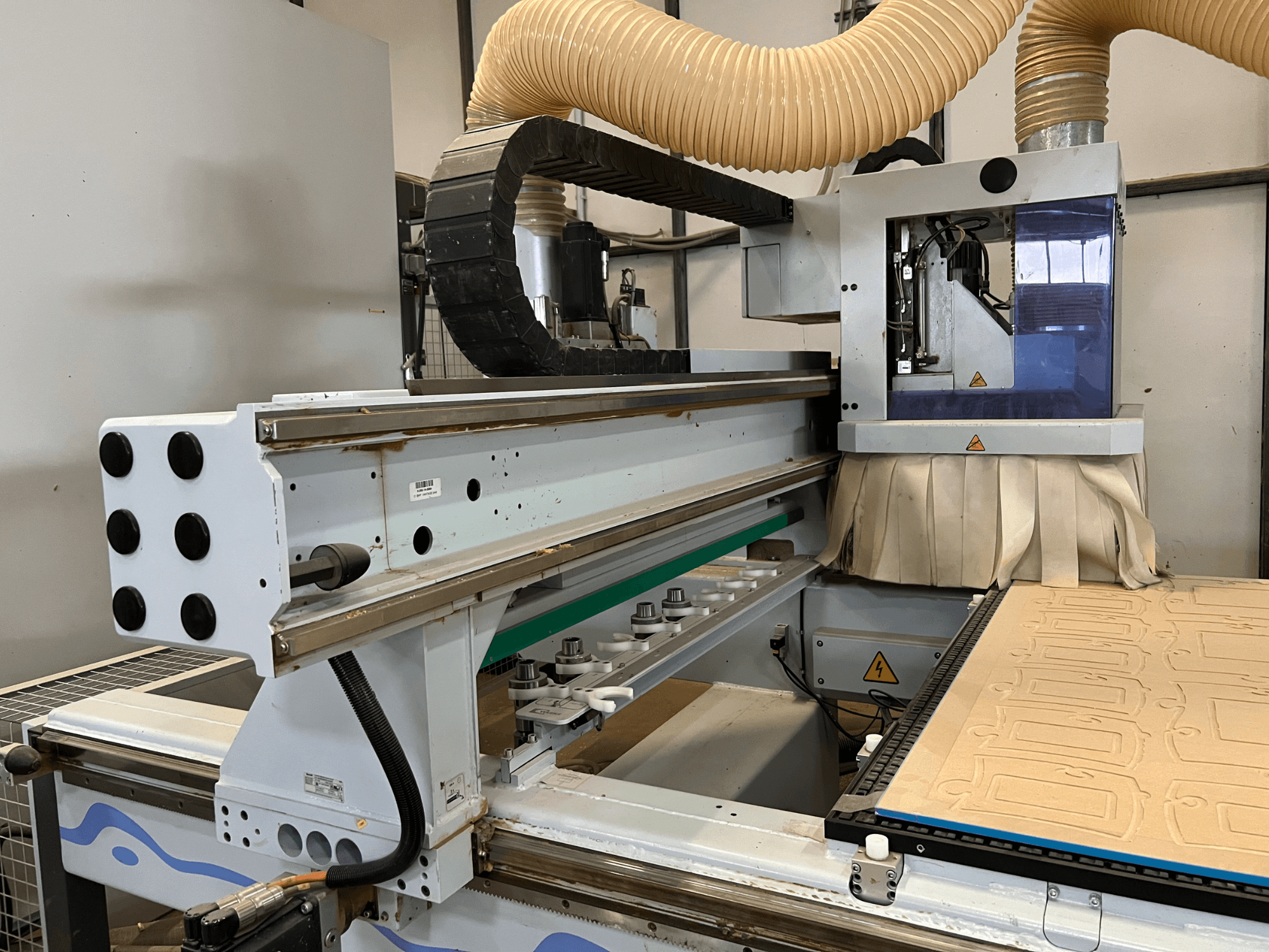 Seitenansicht einer CNC-Fräse mit blauem und silbernem Bedienfeld, ausgestattet mit Staubabsaugung und einem Holzschneidebett.