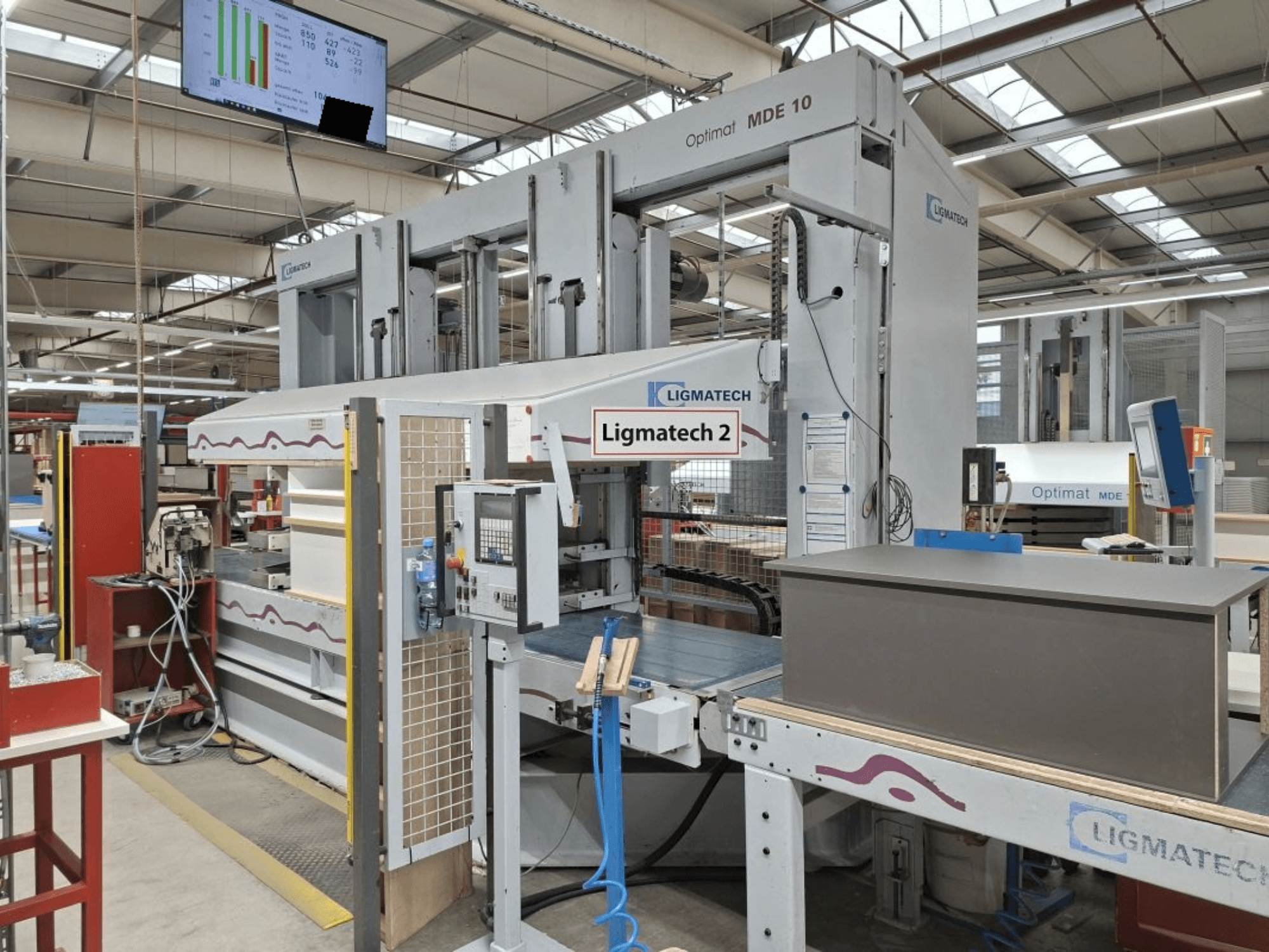 LIGMATECH Optimat MDE 10 Maschine in einer Werkstatt, Seitenansicht mit Bedienelementen und Holzstück auf Förderband.