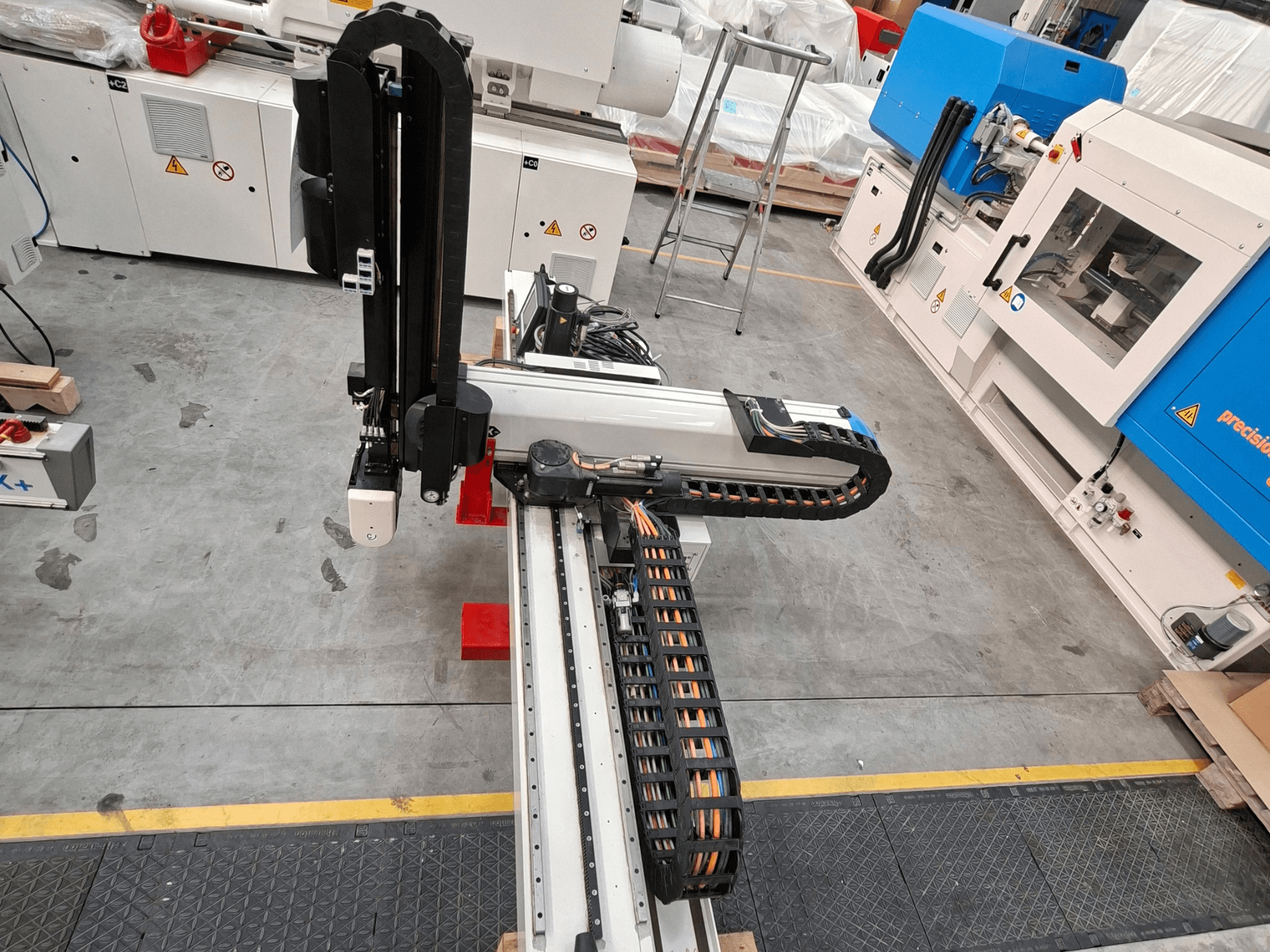 Kunststoffverarbeitungsmaschine Krauss Maffei LRX150-MC5 in der Draufsicht, mit Roboterarm und Kabelkanal in der Fabrikhalle.
