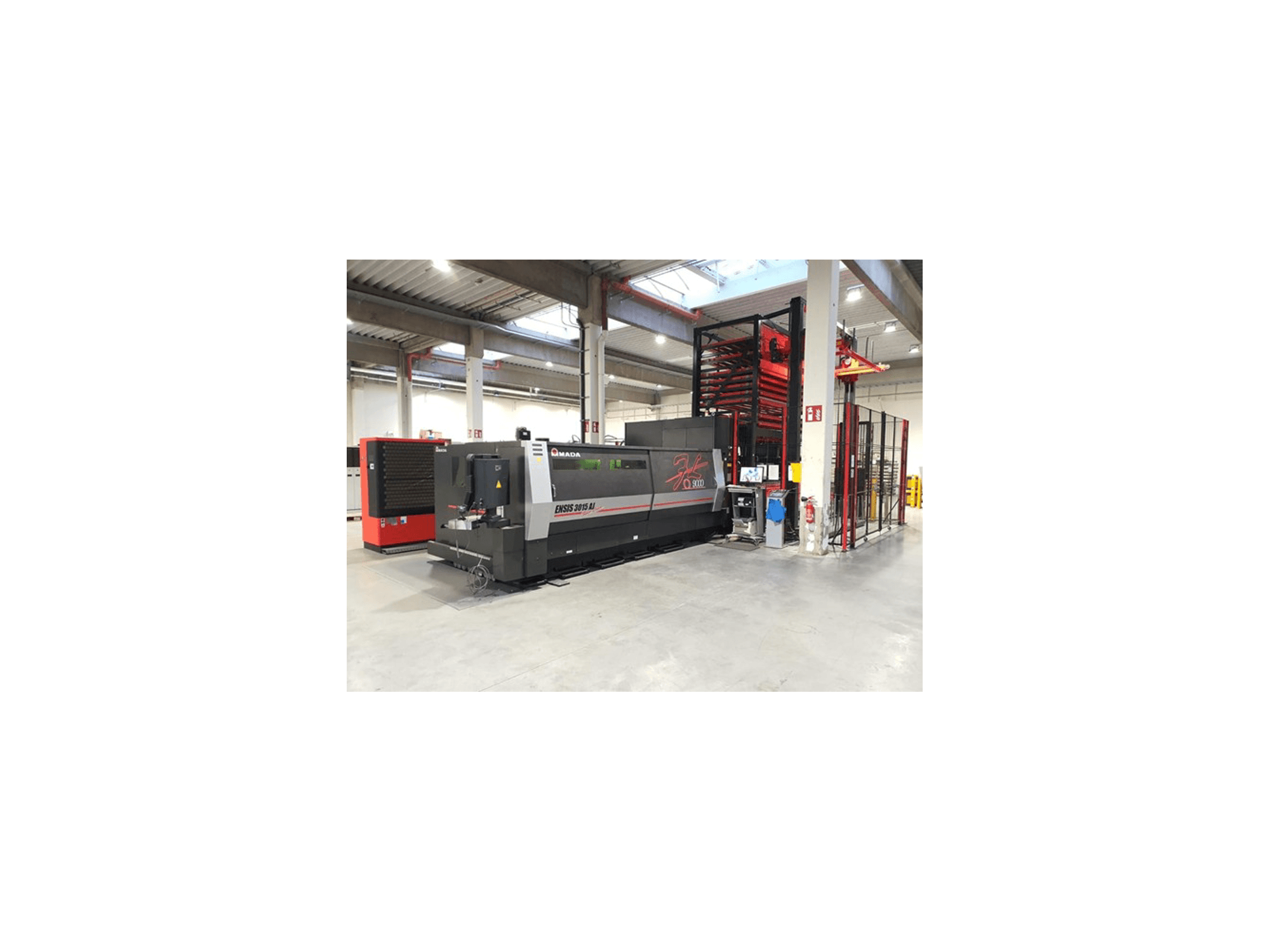 Amada ENSIS 3015 Aj Laserschneidmaschine aus der Vorderansicht, aufgestellt in einer geräumigen Industriehalle mit Metallregalen.