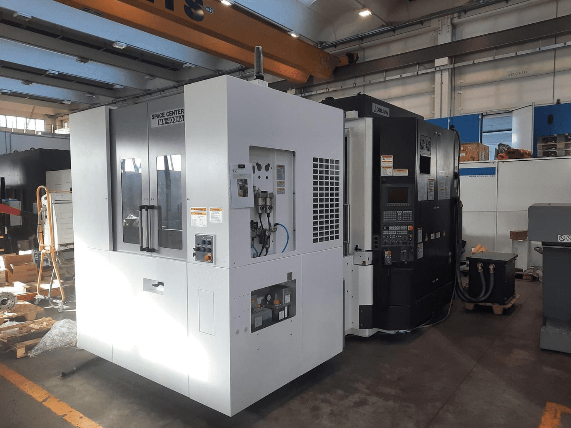 Frontansicht der CNC-Maschinen SPACE CENTER IM-400HAA und OKUMA mit verschiedenen Steuerungen und Herstelleretiketten.