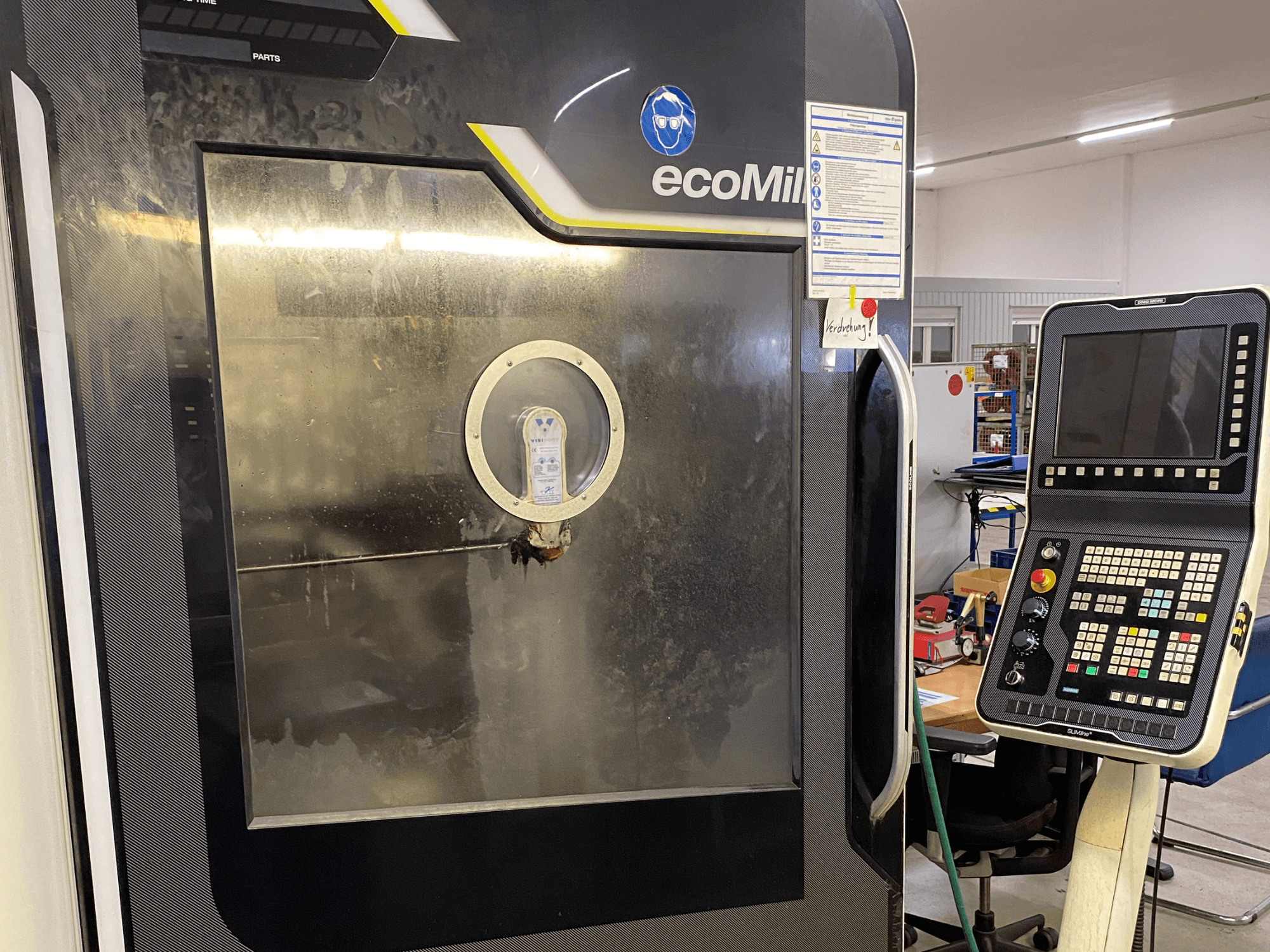 DMG MU 70 ECO-Fräsmaschine in Vorderansicht, mit einem Bedienfeld auf der rechten Seite und einer Glasabdeckung, die den Blick auf die inneren Bauteile freigibt.