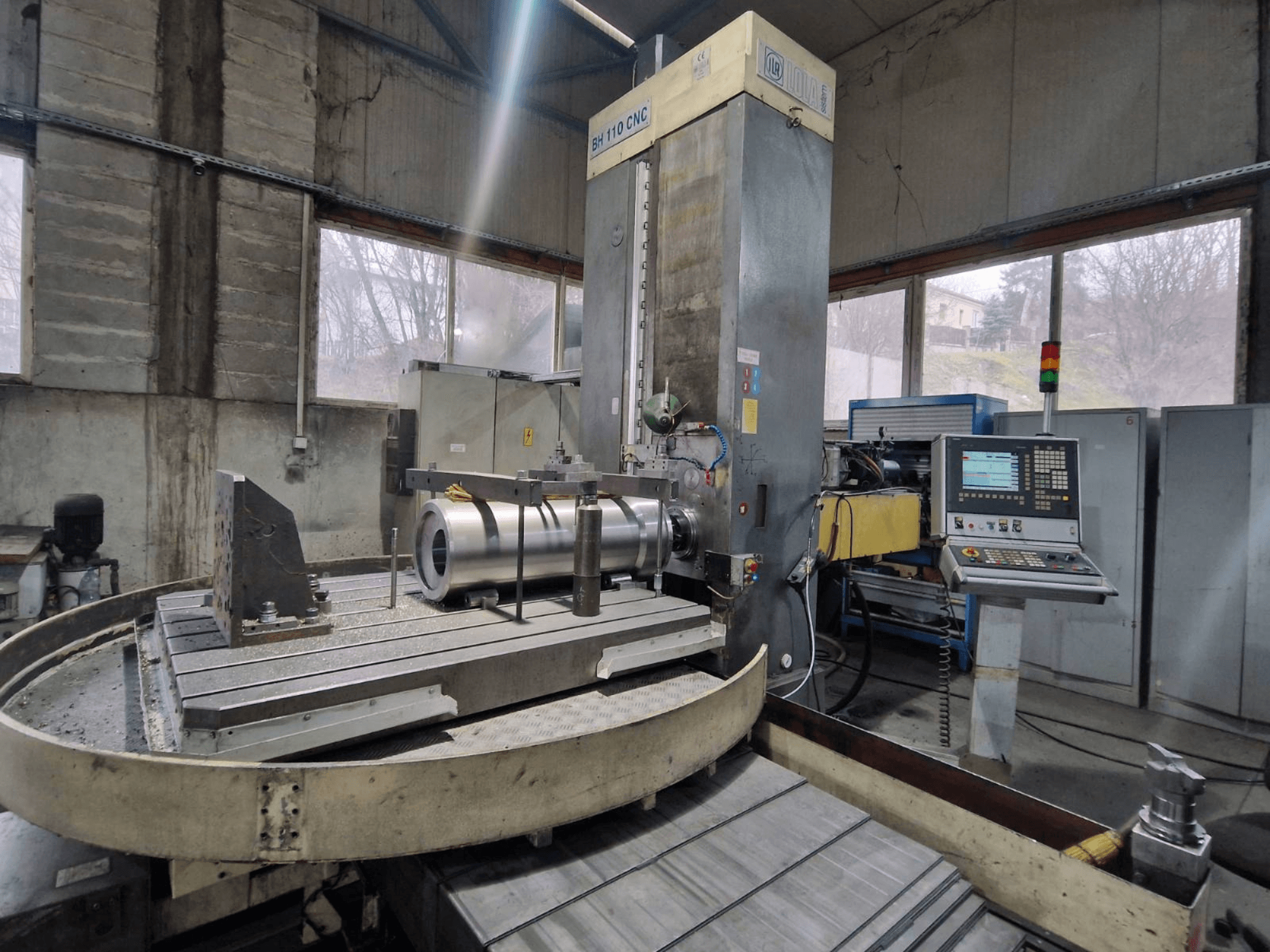 LOLA BH 110 CNC-Bohrmaschine in einer Werkstatt, Vorderansicht, mit Metallwerkstück und Bedienfeld.