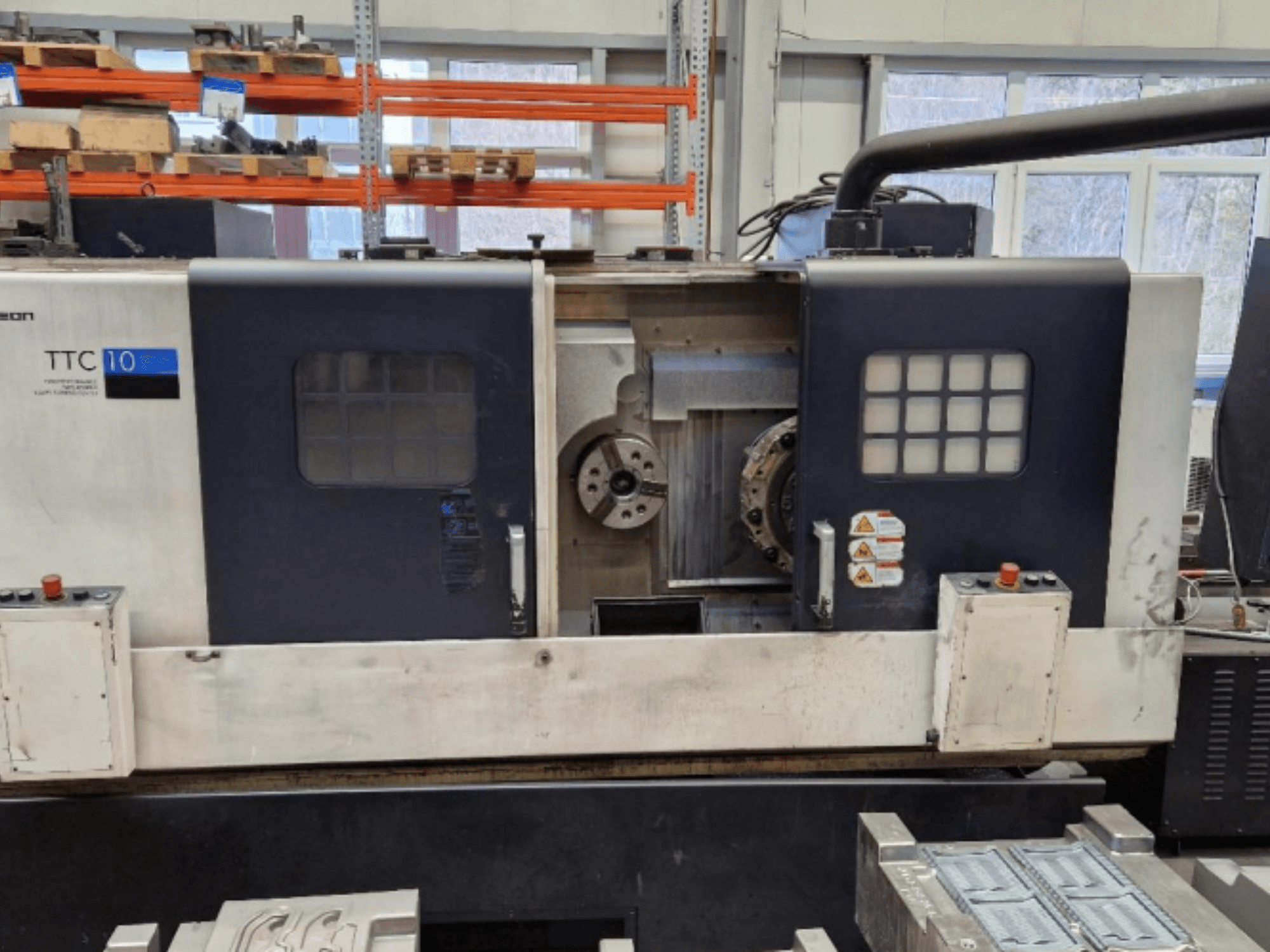 Vorderansicht der Drehmaschine TTC 10 mit Bedienfeld, sichtbaren Spannfuttern und Arbeitsbereich mit Metallteilen.