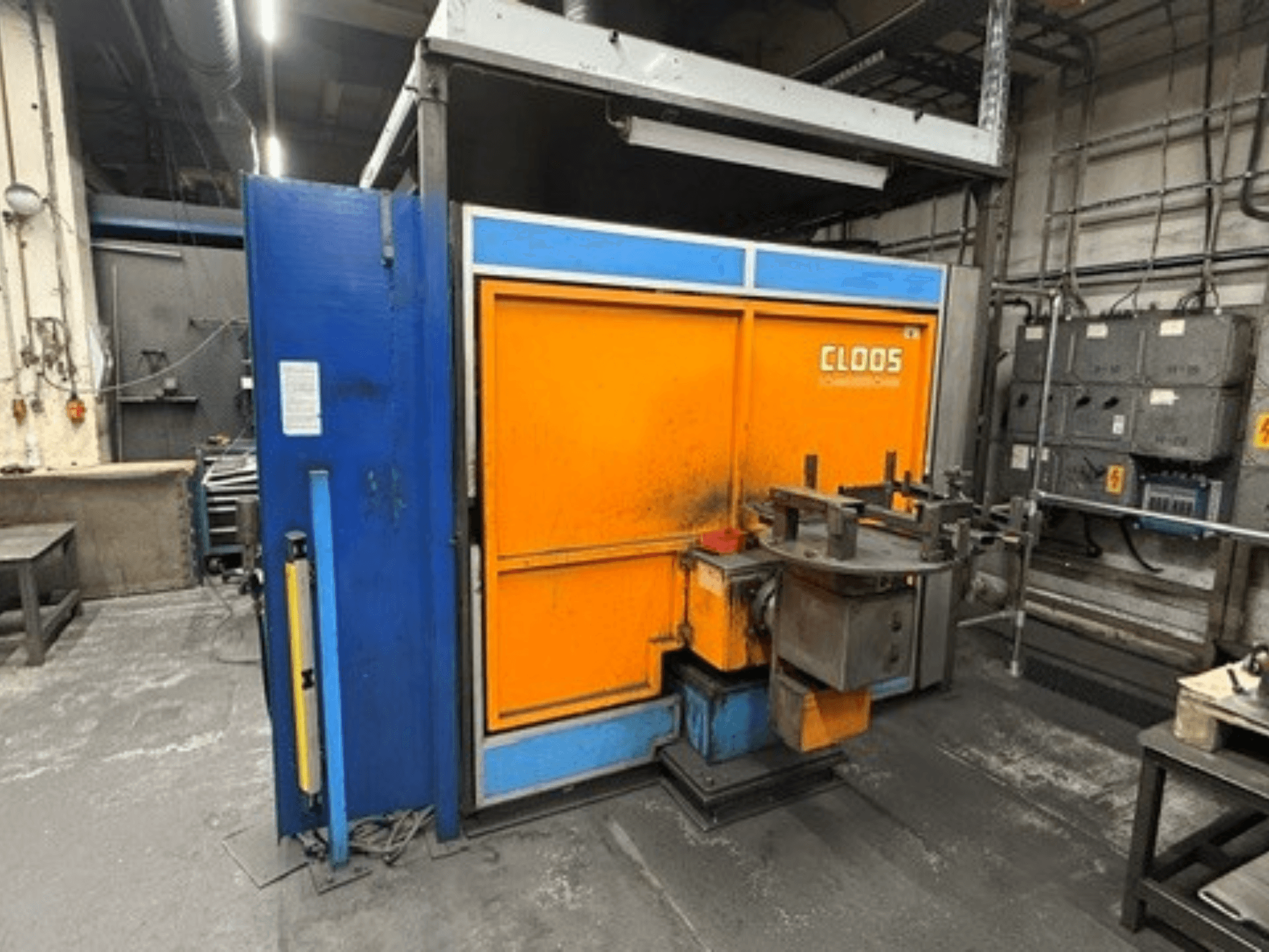 CLOOS Romat 320-Schweißroboter in einer Werkstatt, Vorderansicht mit orange-blauer Verkleidung, Bedienfeld und Werkzeugen.
