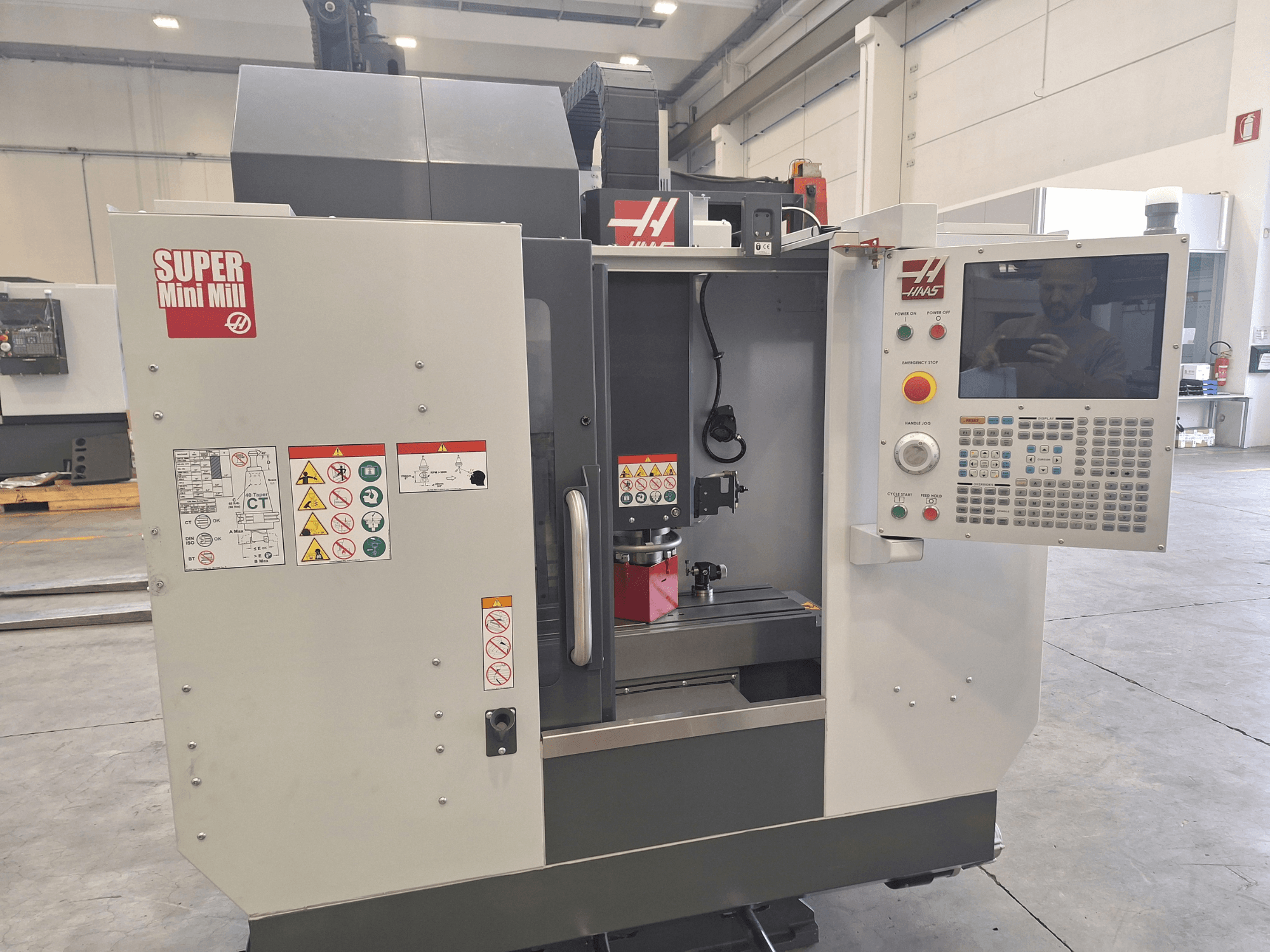 Vorderansicht der HAAS Super Mini Mill mit Bedienfeld, Sicherheitshinweisen und Bearbeitungsbereich mit einem eingespannten Werkstück.
