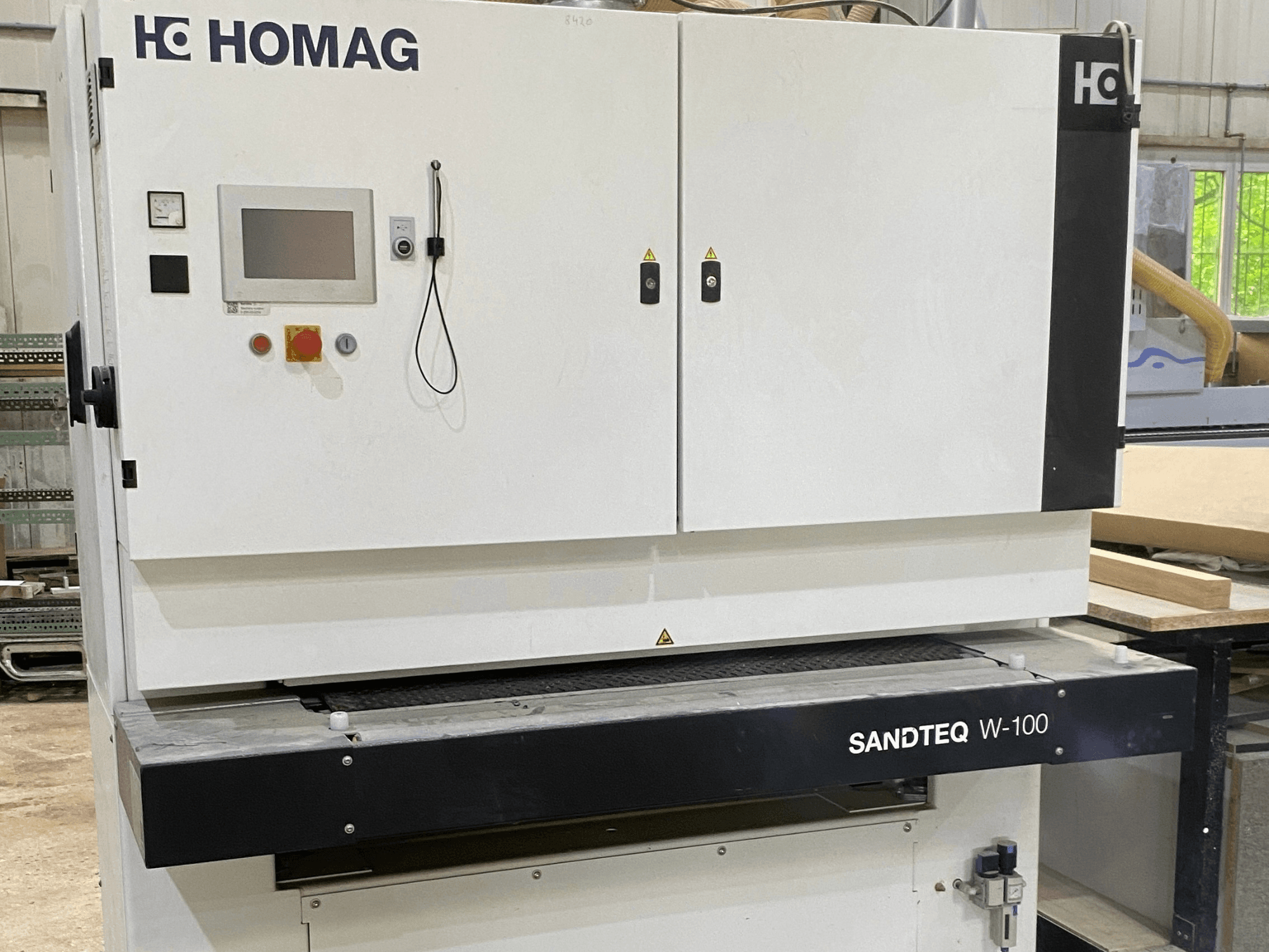 HOMAG SANDTEQ W-100 Bandschleifmaschine in einer Werkstatt, mit Blick auf das Bedienfeld, den Staubanschluss und den Schleifbandbereich. Vorderansicht.