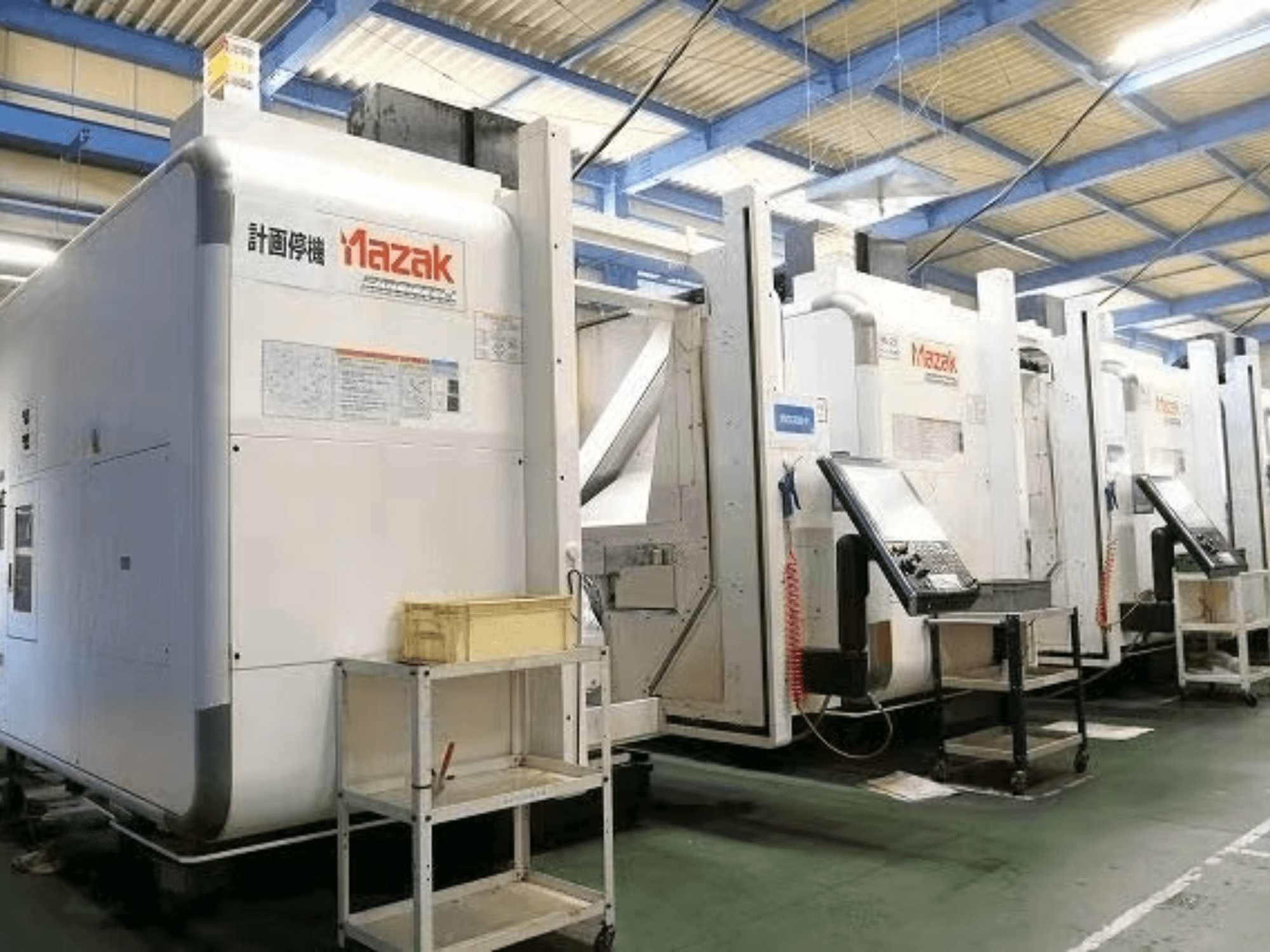 Mazak CNC-Maschinen in einer Fabrikumgebung, Seitenansicht mit Bedienfeldern und Etiketten auf weißen Gehäusen.